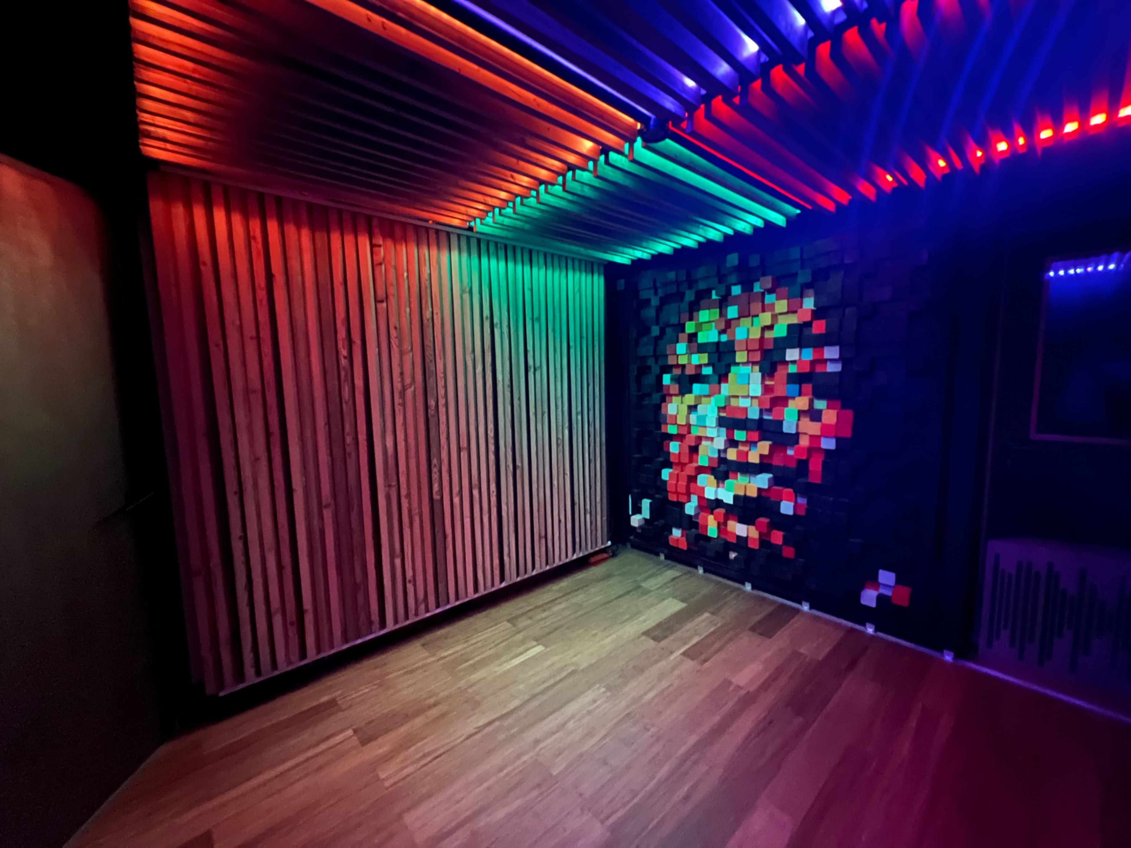 The room features wooden walls and a colorful illuminated ceiling, with a pixel art mural on one wall.