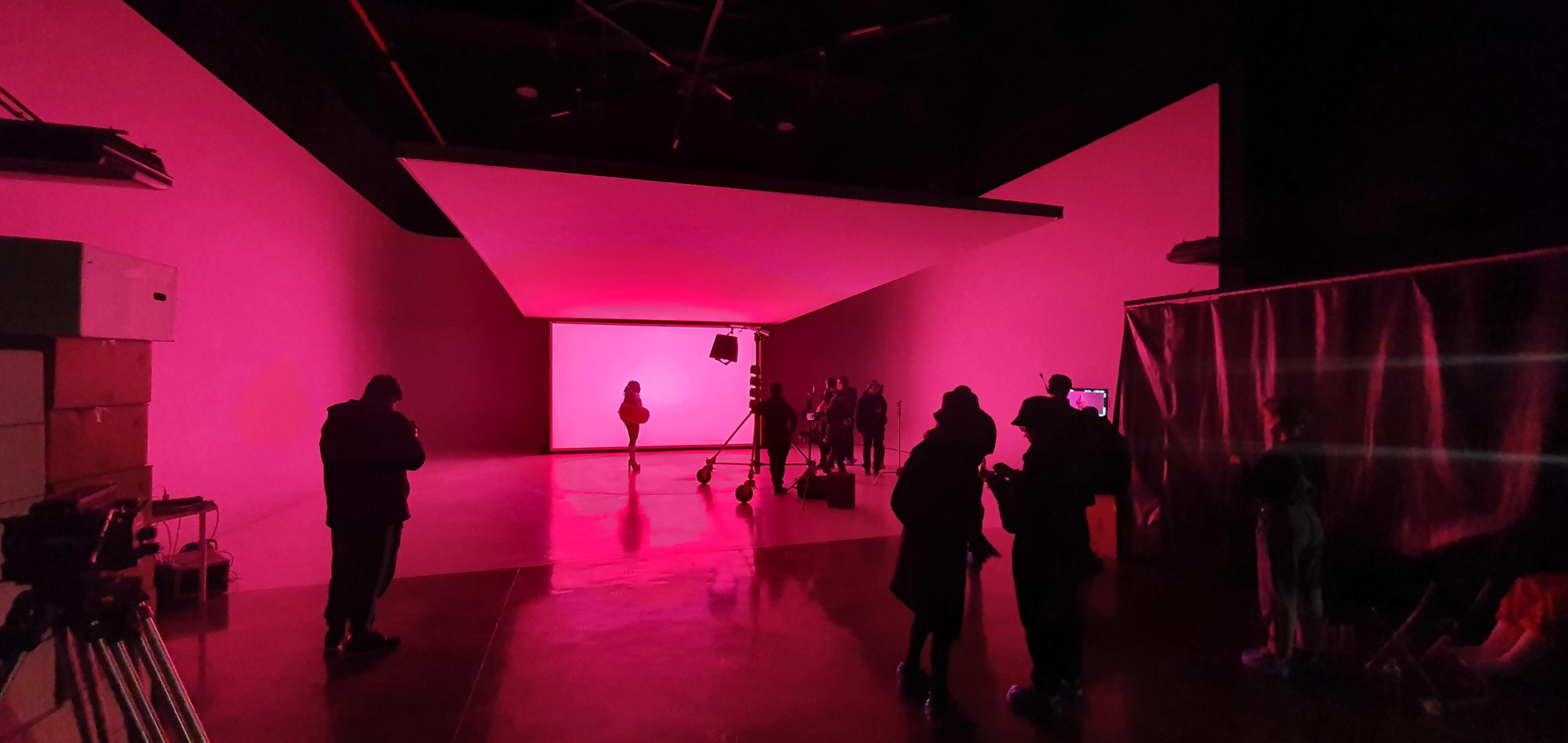 A group of people prepares for a shoot in a studio illuminated with pink lighting.
