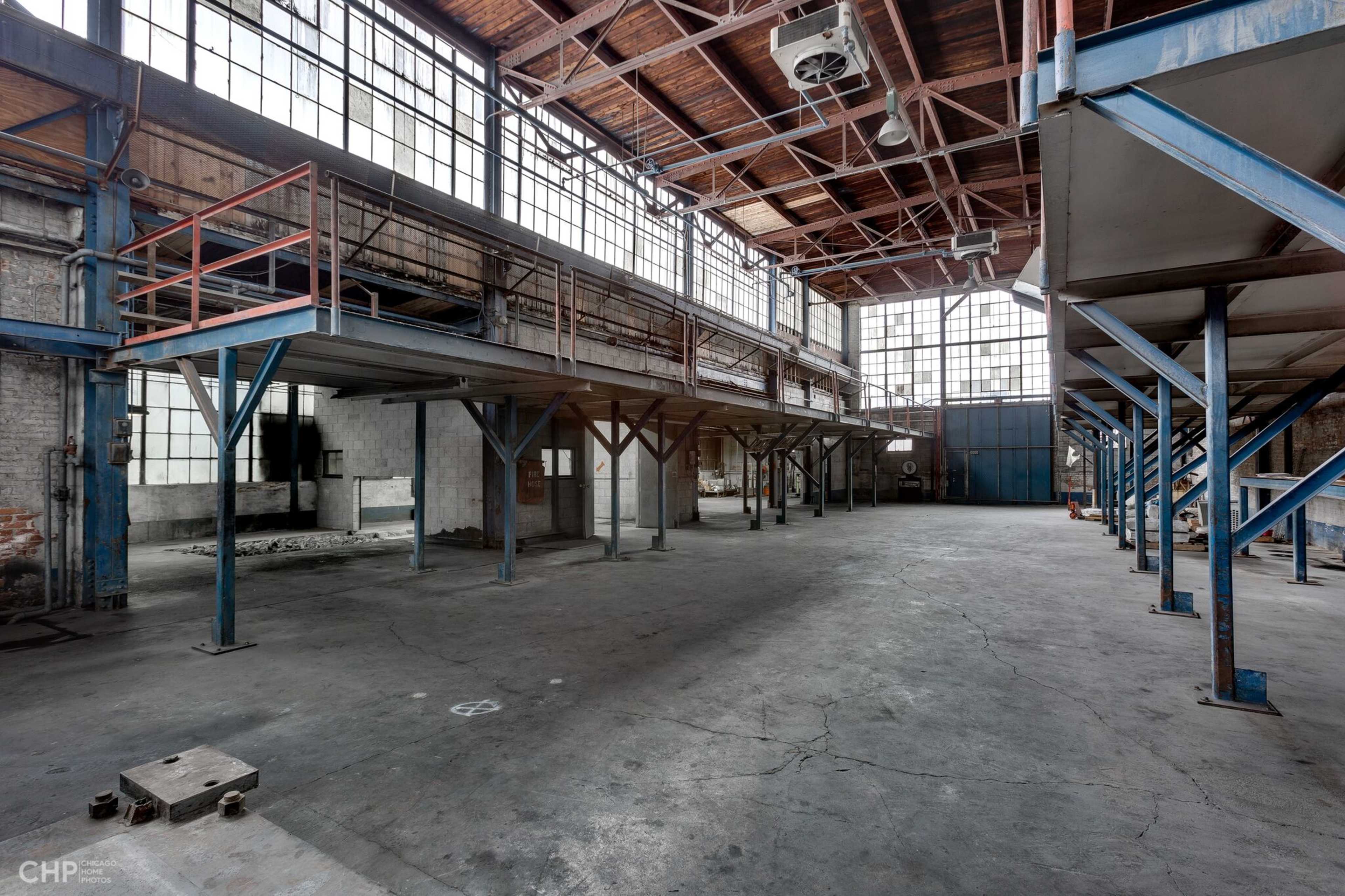 An empty industrial space with high ceilings, large windows, and metal support beams.