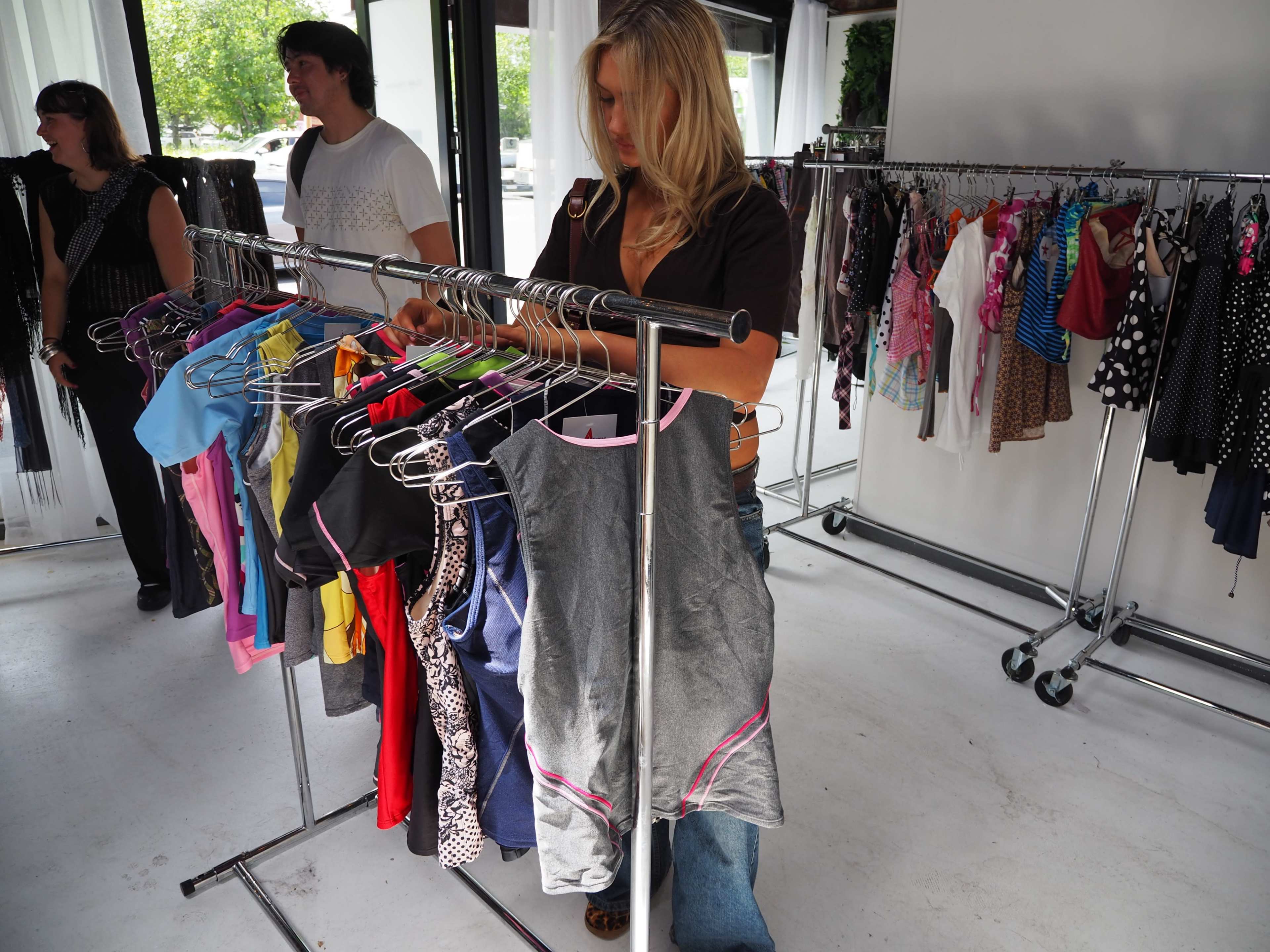 A woman inspects clothes on a rack while others browse nearby in a boutique setting.