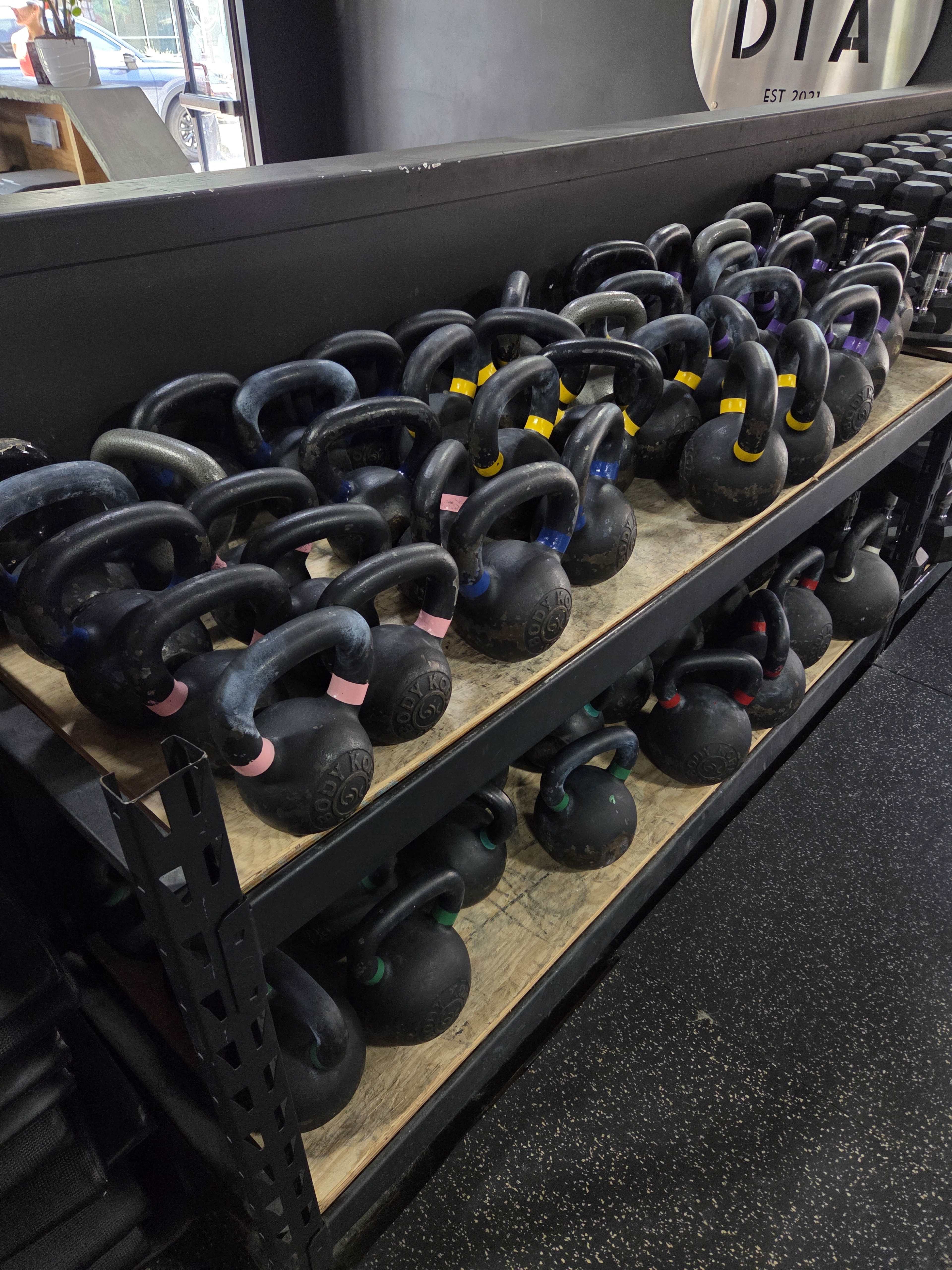 A row of kettlebells in various weights is neatly arranged on shelves in a gym.