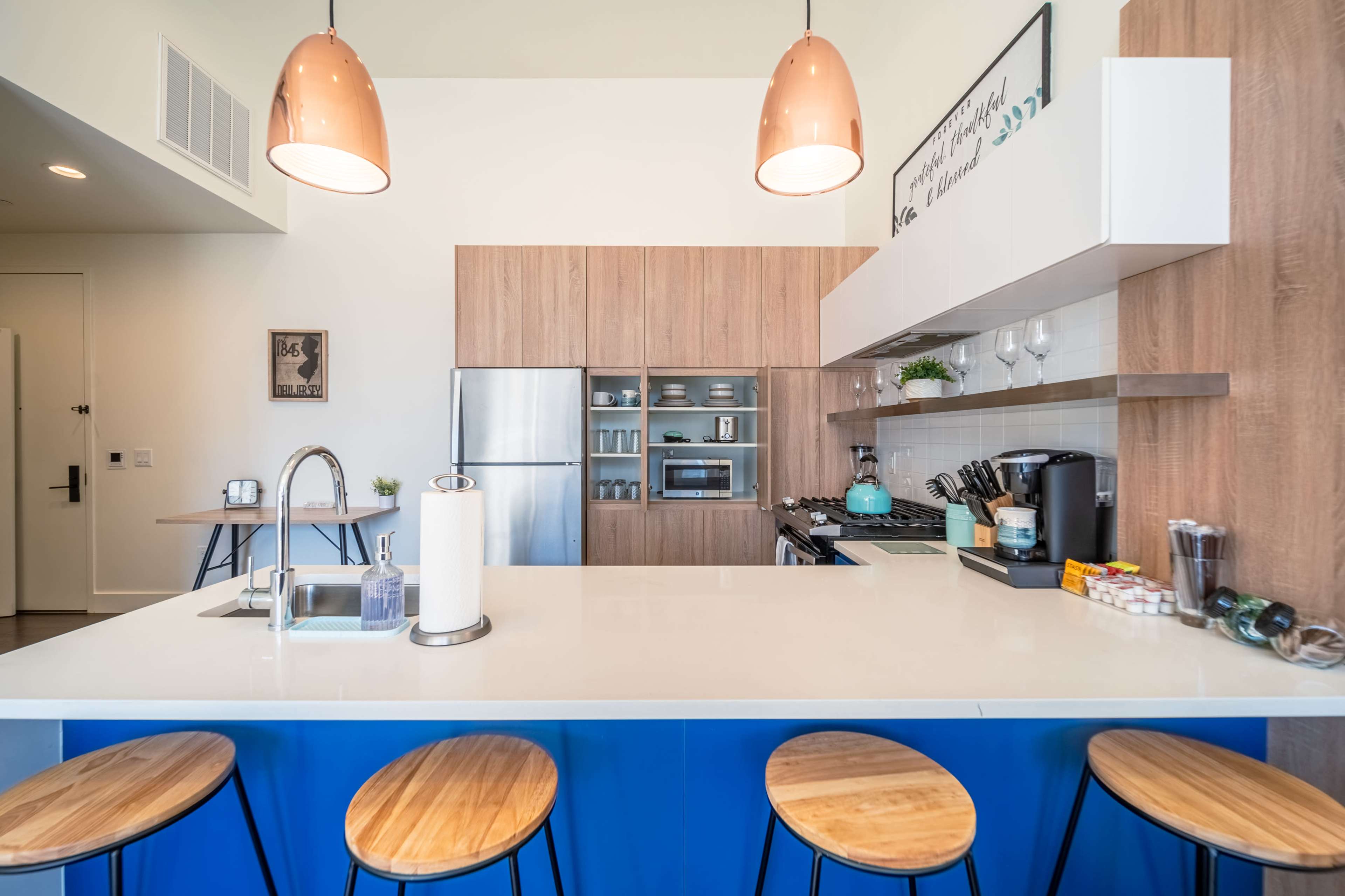 A modern kitchen with wood cabinetry, stainless steel appliances, and a blue island featuring wooden bar stools.