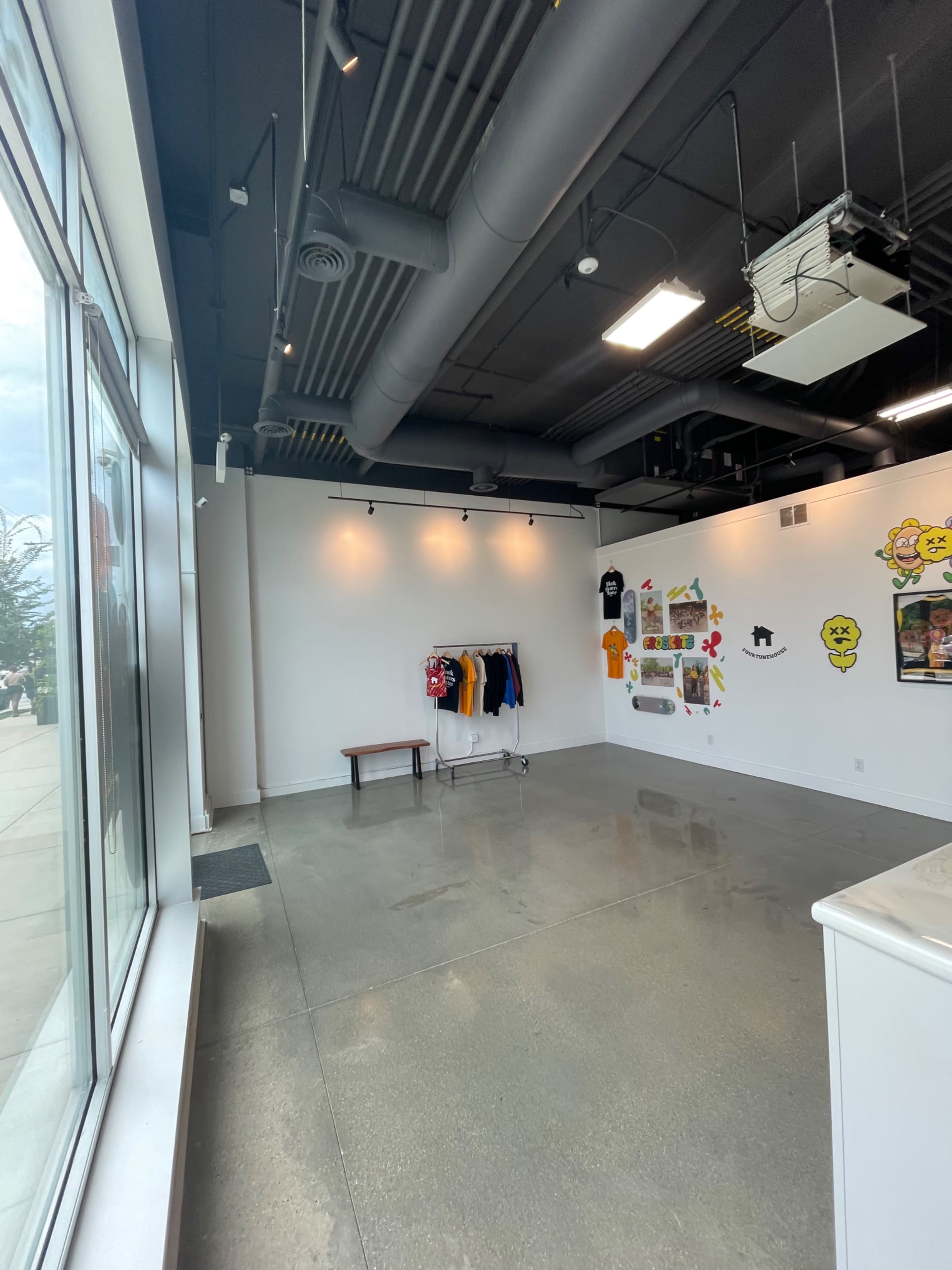 A spacious, empty room with a clothing rack, a bench, and a wall decorated with colorful art and graphics.