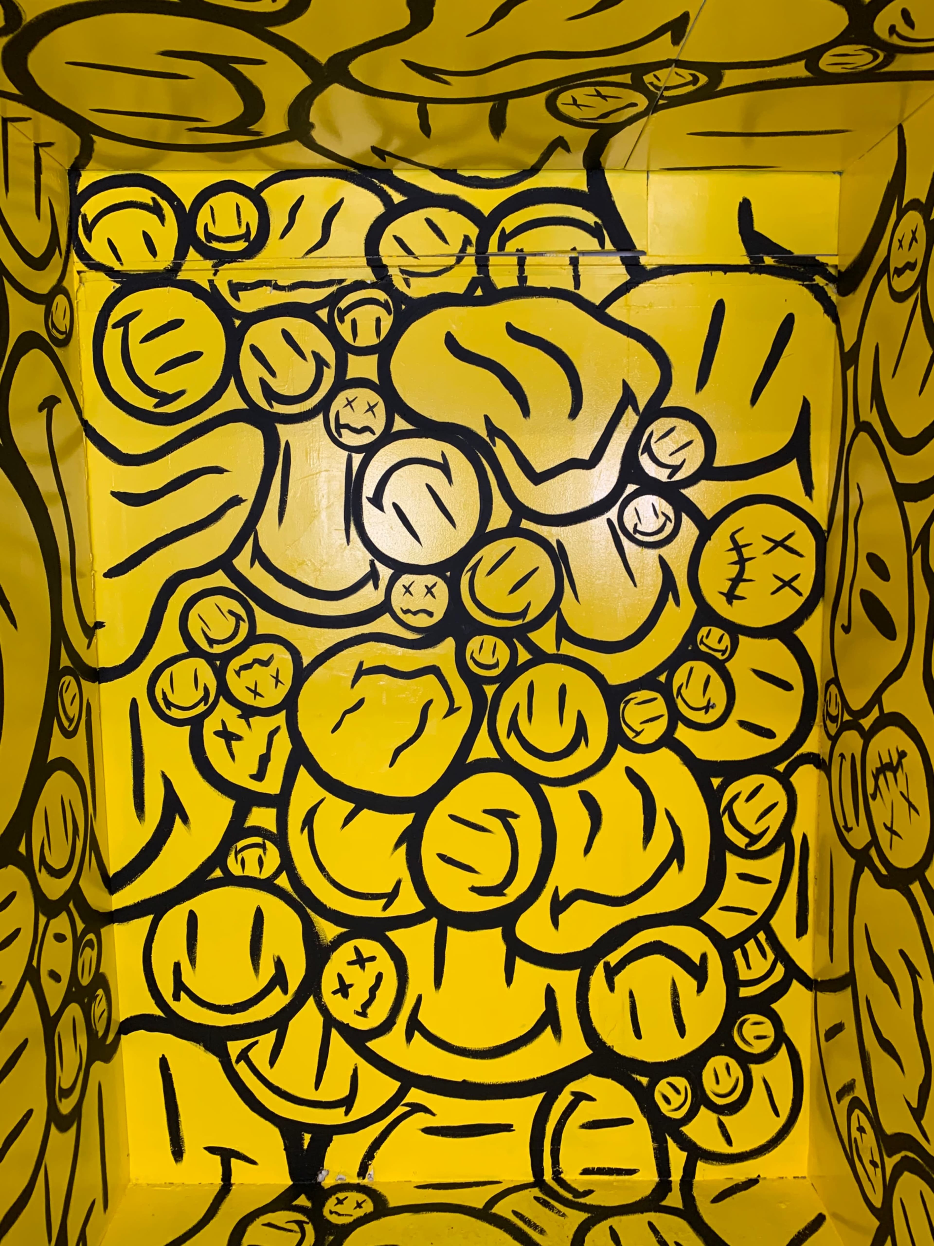 A small space with walls covered in yellow paint and black smiley face and emoticon designs.