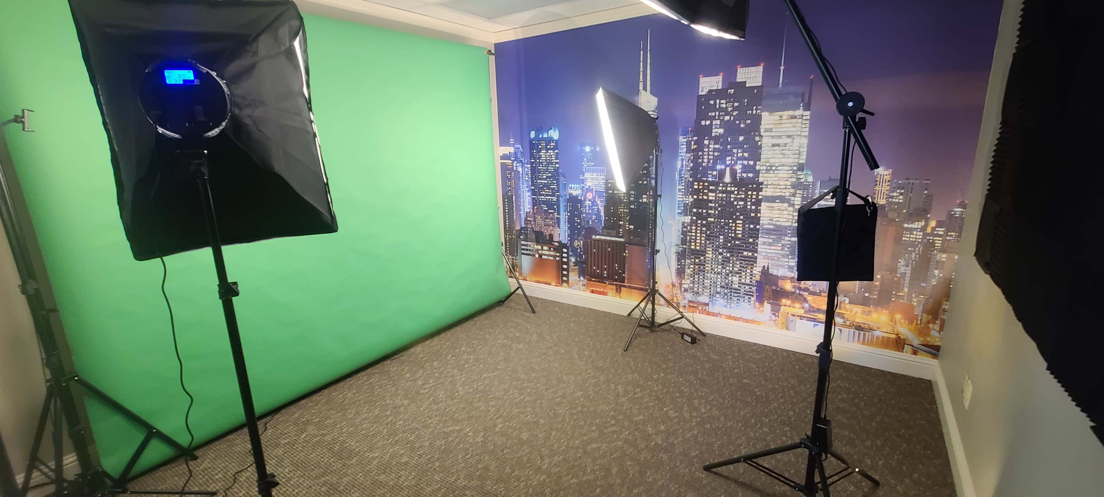 A studio setup with a green screen, two softbox lights, and a backdrop of a city skyline at night.
