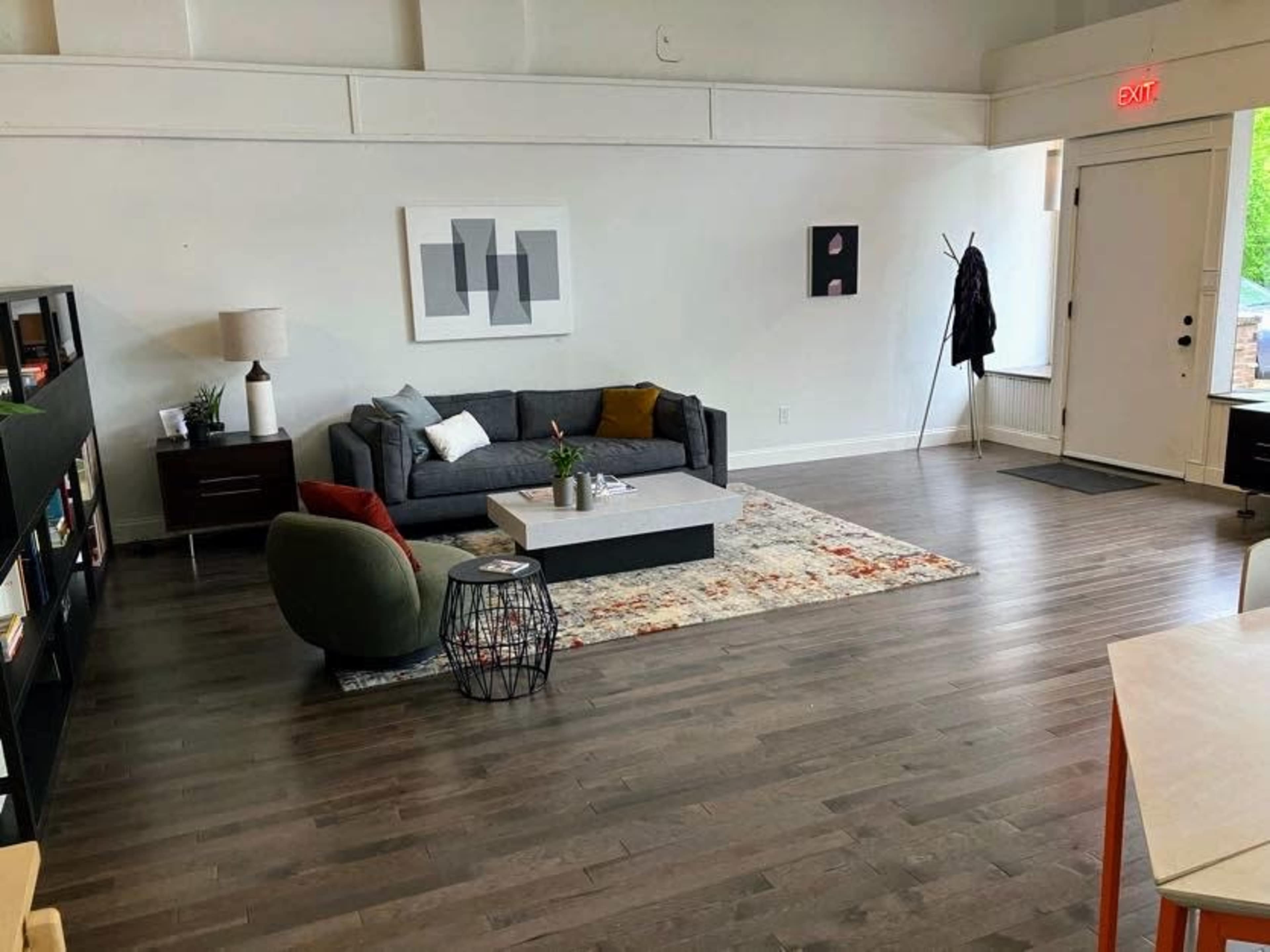 A modern living room features a gray sofa, a coffee table on a patterned rug, and a bookshelf, with a door leading to the outside.