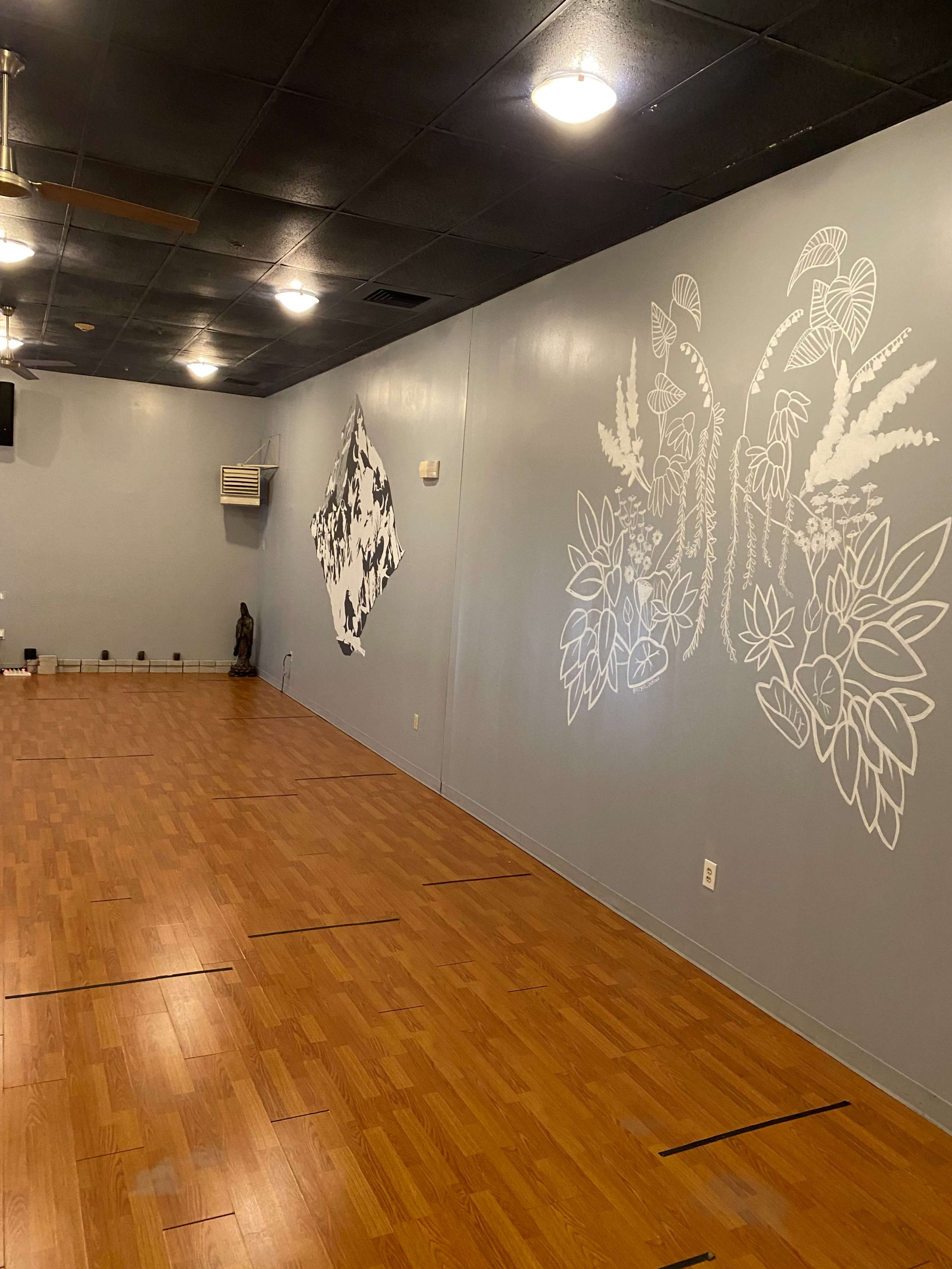 The interior of a studio features wooden flooring and light blue walls decorated with white botanical murals.