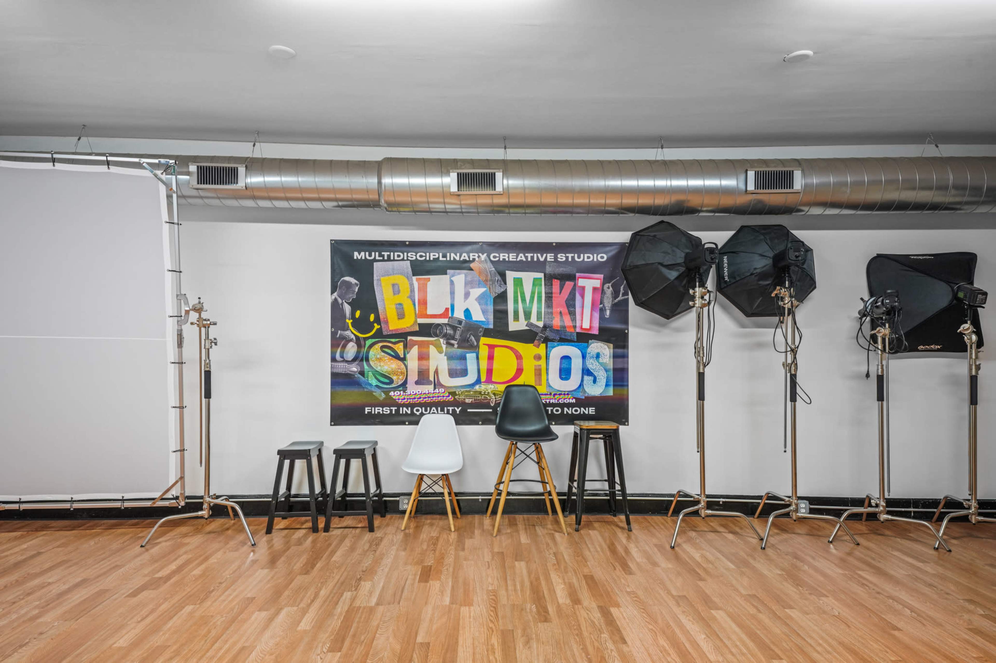 A creative studio space with a large colorful banner, various studio lights, and a row of stools against a wooden floor.