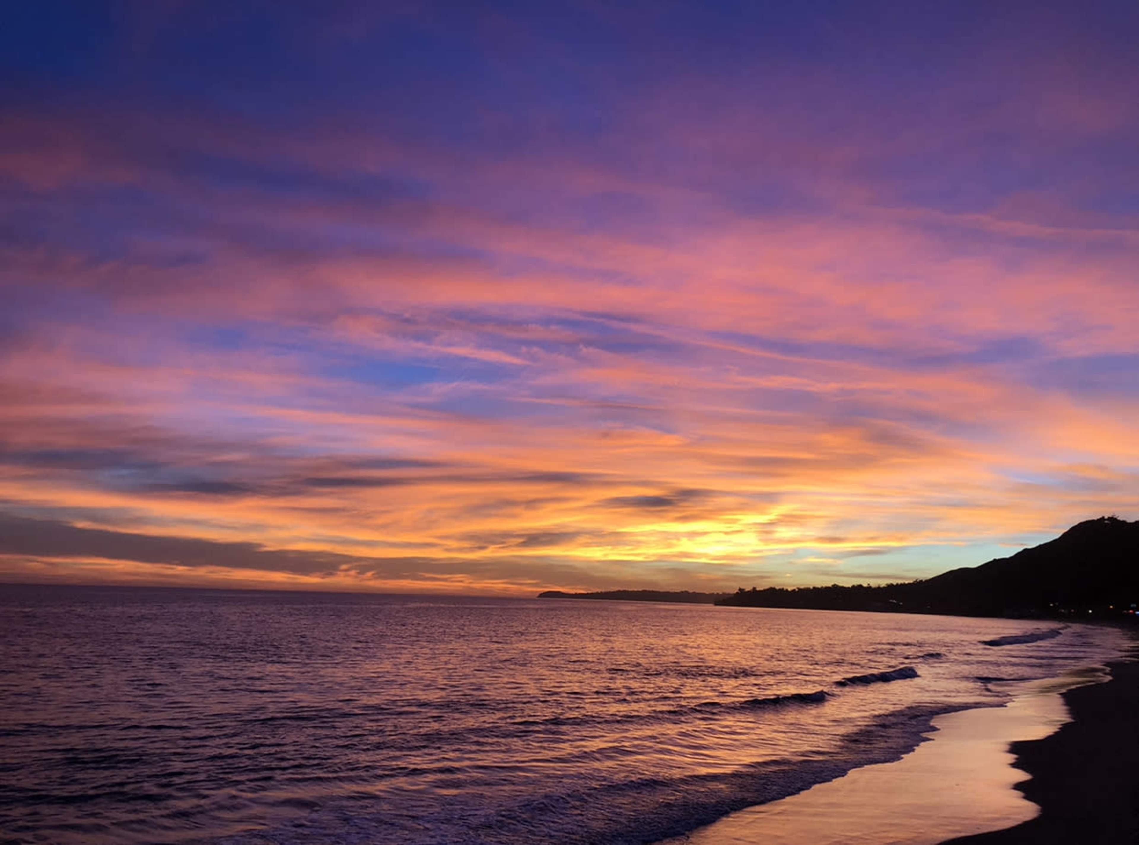 A beach at sunset, with vibrant colors in the sky reflecting on the water.