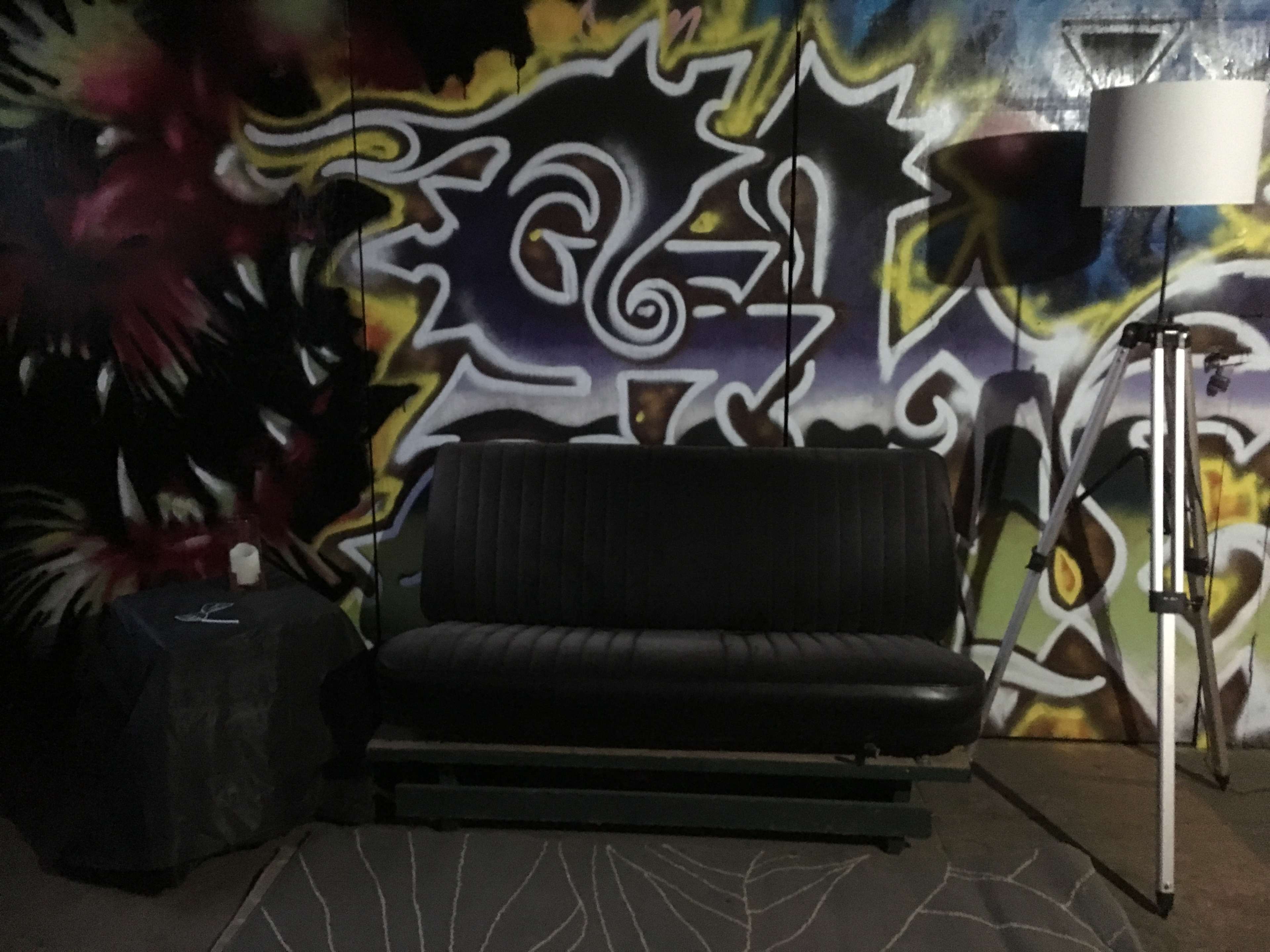 The scene features a black sofa in front of a colorful graffiti wall, accompanied by a small table and a floor lamp.