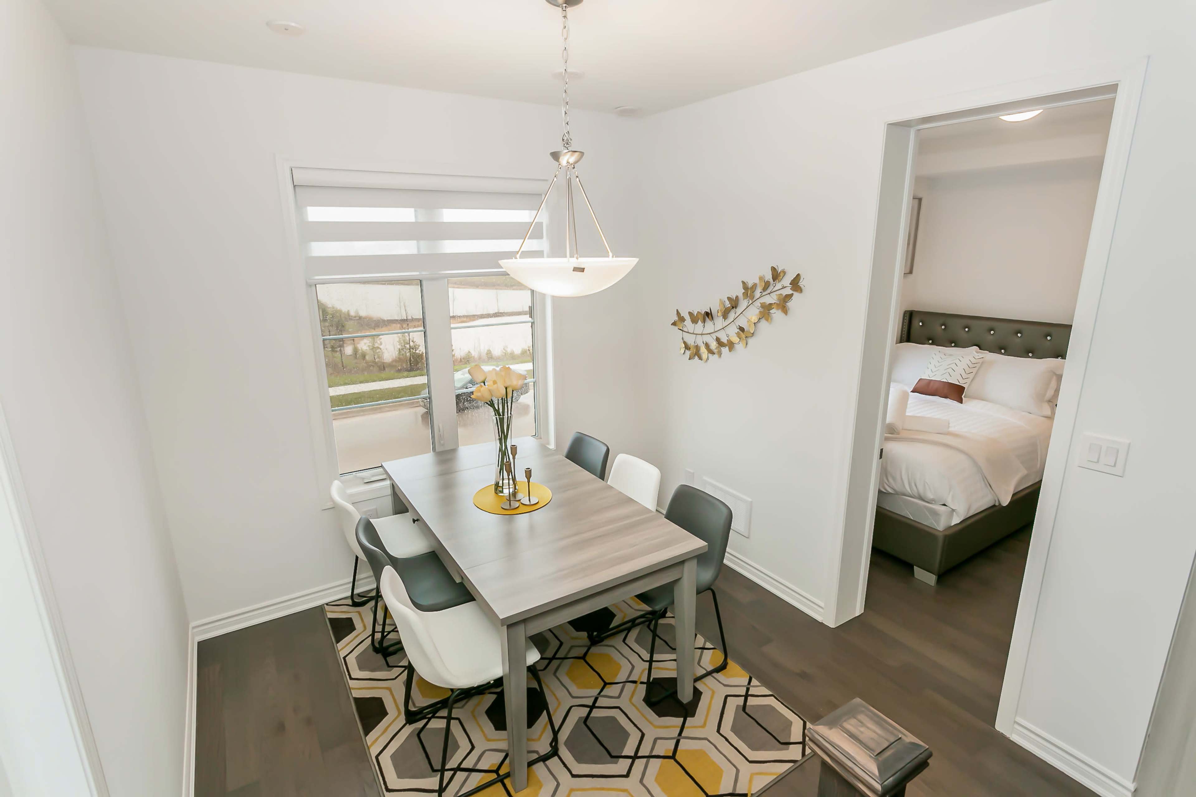 A dining area features a table with six chairs, a pendant light above, and a large window overlooking a landscape, complemented by a hexagonal-patterned rug.