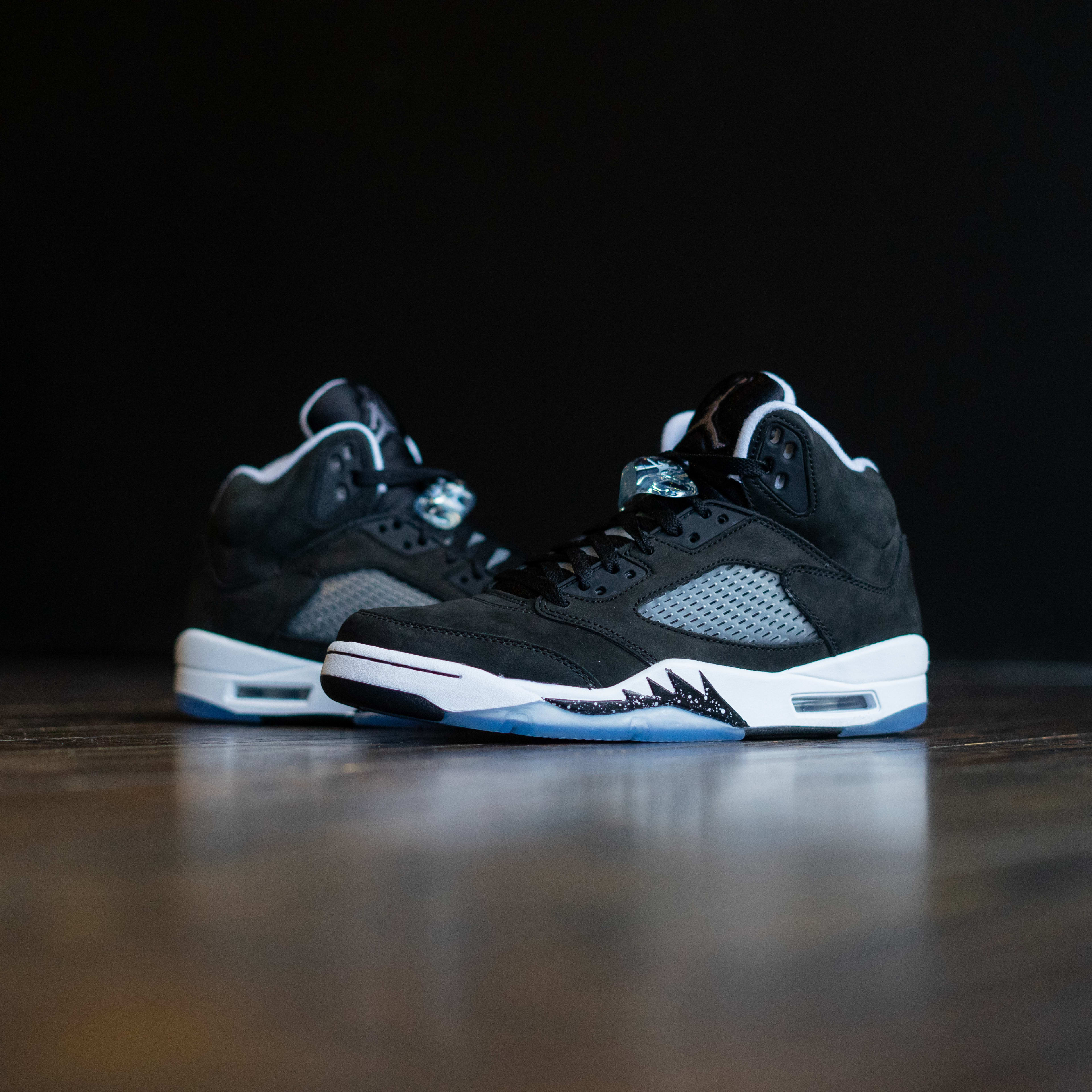 A black pair of sneakers placed on a wooden floor for a photoshoot.