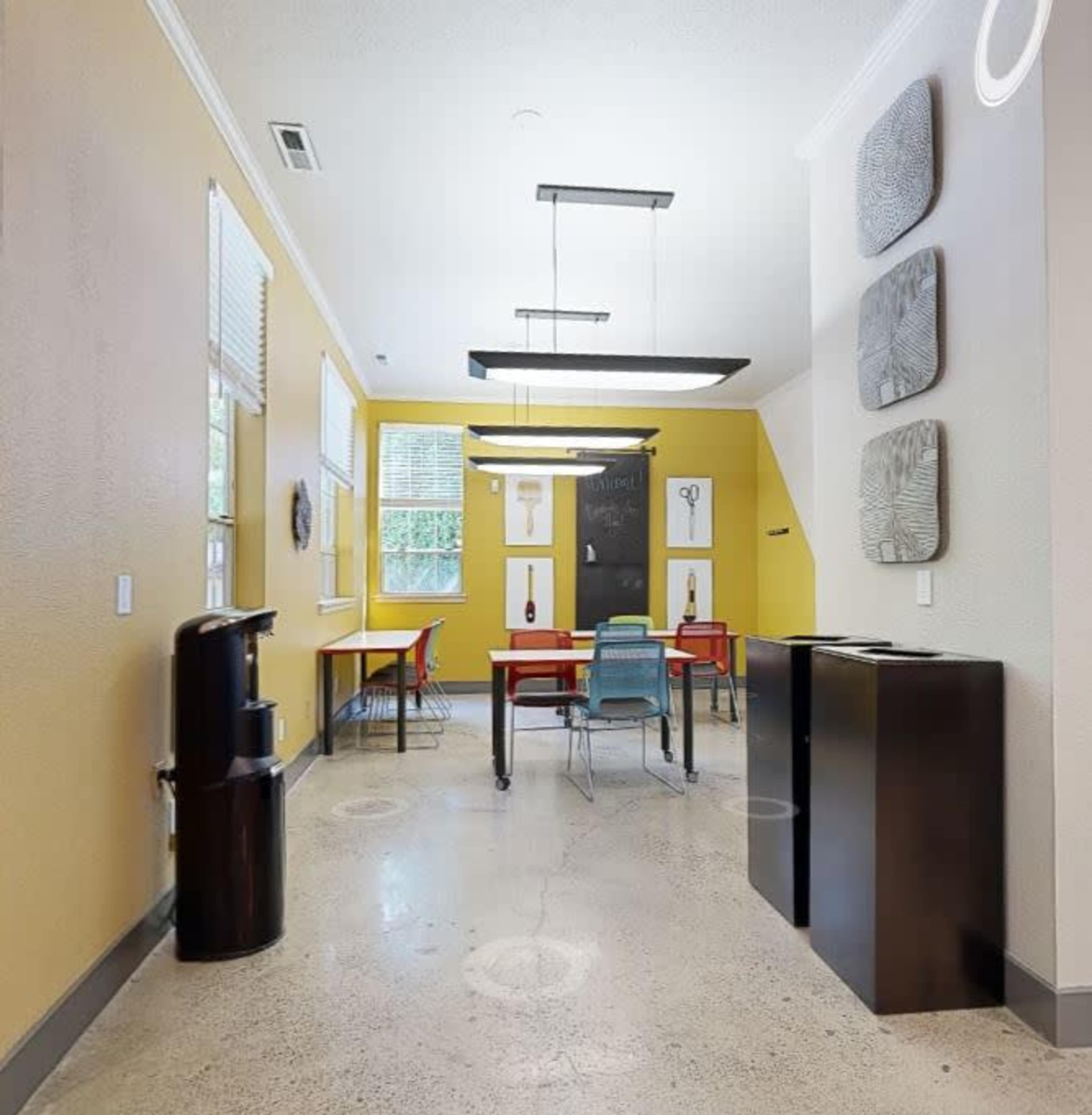 A brightly colored room with a small dining area featuring a red table, metal chairs, and wall art, set against a yellow wall.