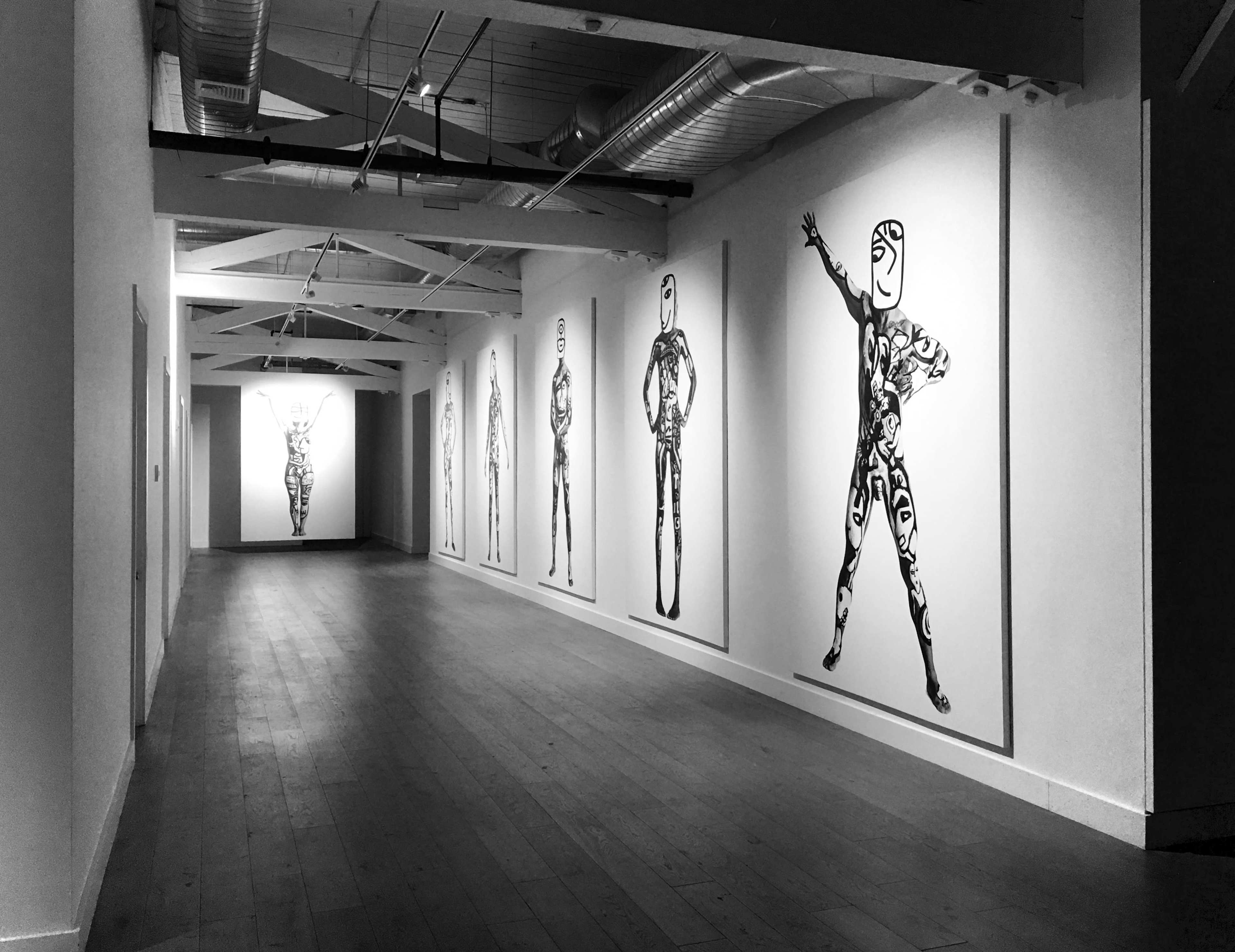 A long, narrow gallery features several large black and white artworks of stylized human figures on the walls.