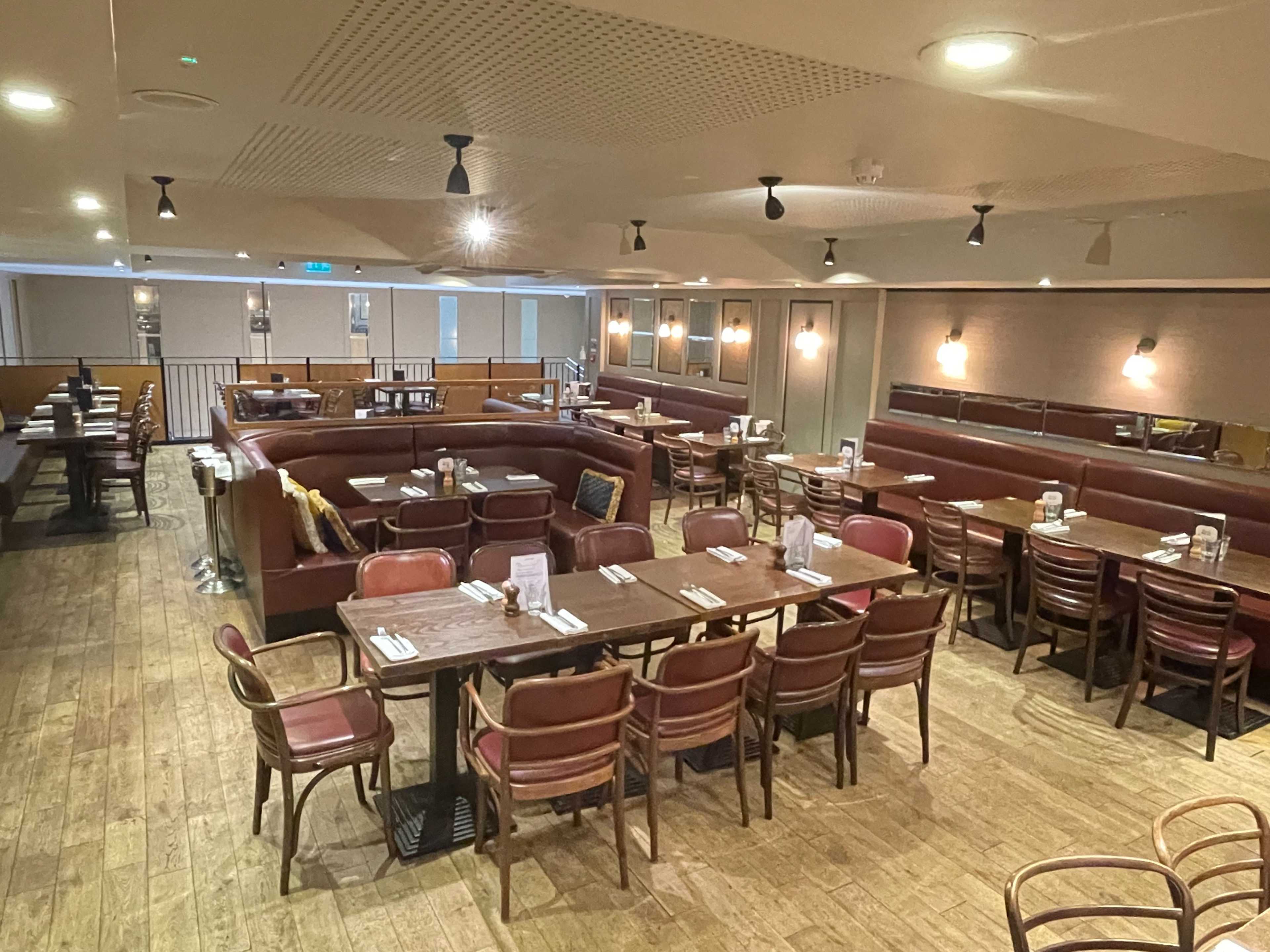 The image shows a spacious restaurant interior featuring wooden floors, several dining tables with chairs, and a combination of booth and standard seating arrangements.