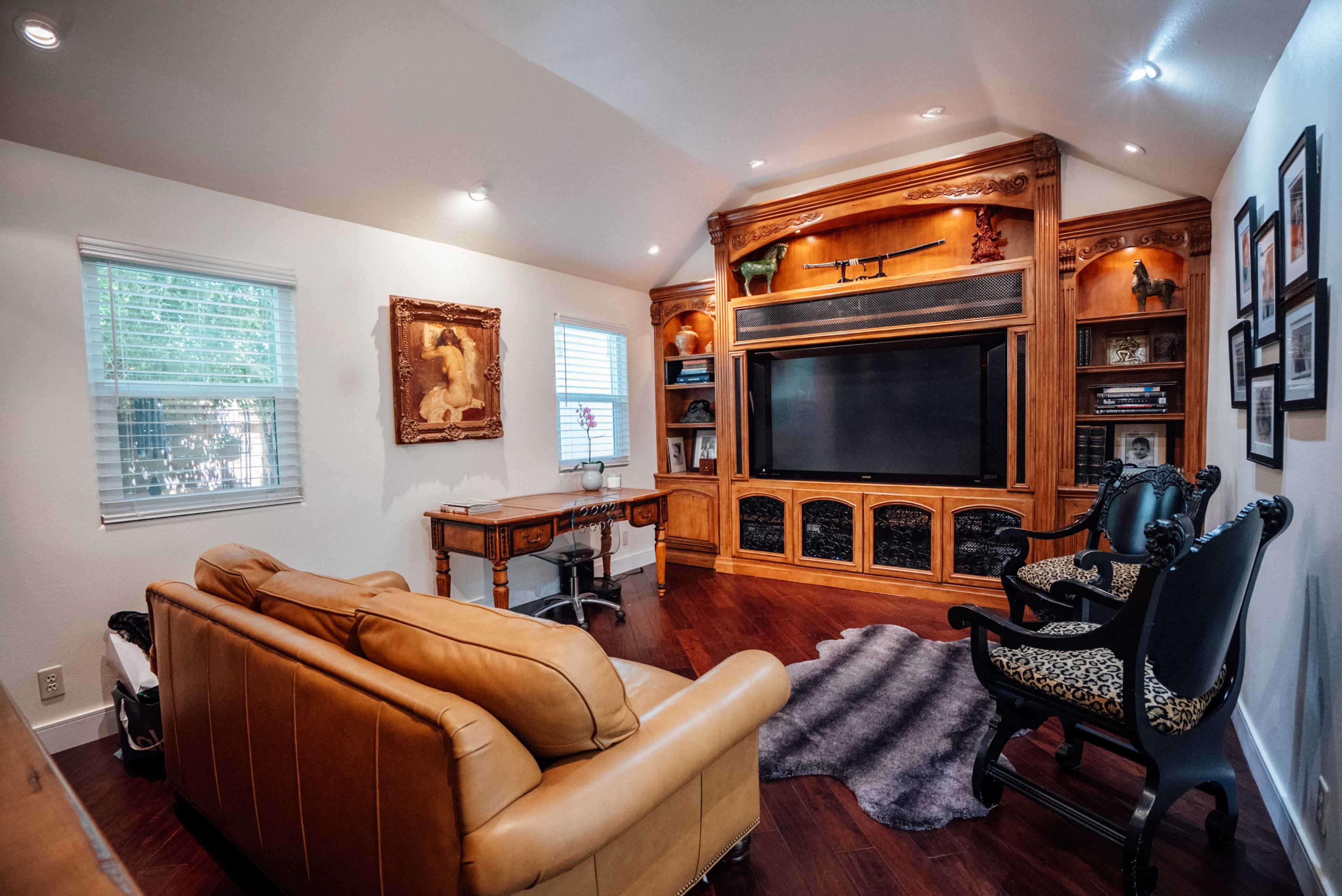 The image shows a cozy living room with a leather couch, a wooden entertainment center, and a desk, complemented by decorative accents on the walls.