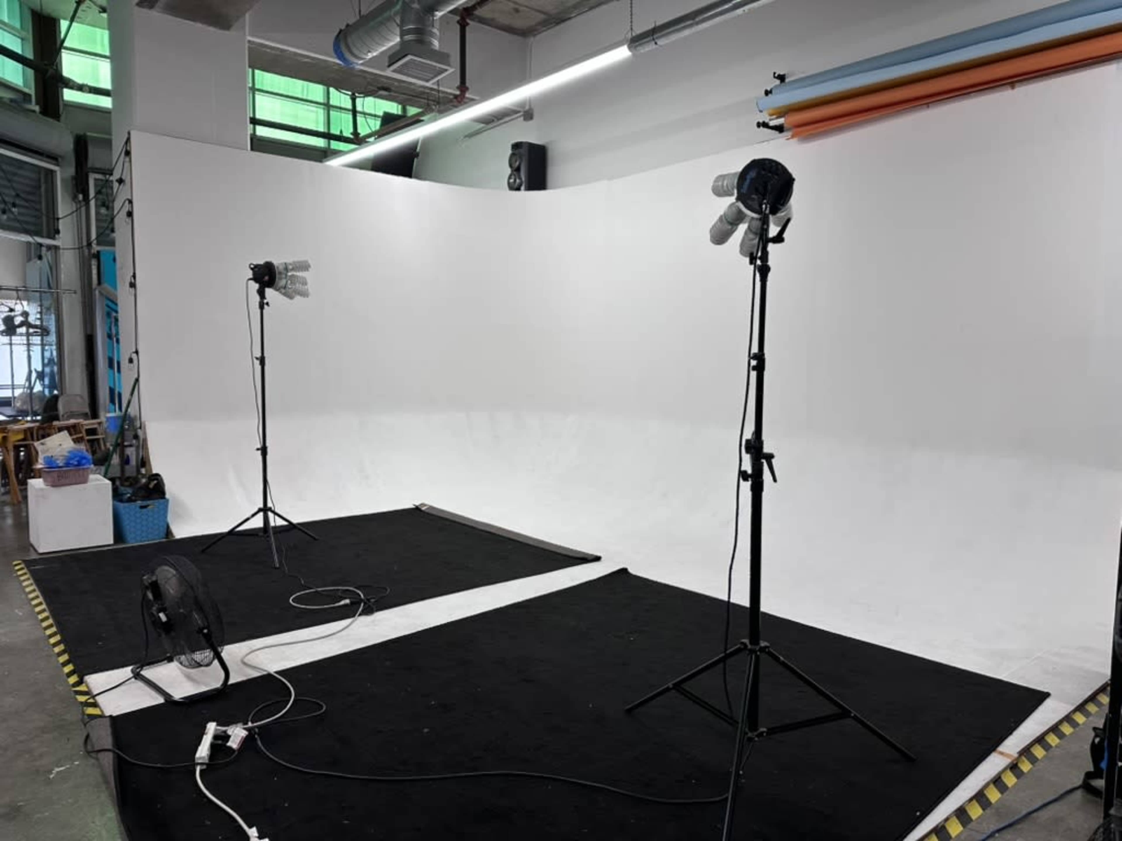The image shows a photography studio setup with a curved white backdrop, two studio lights on stands, and a black carpet.