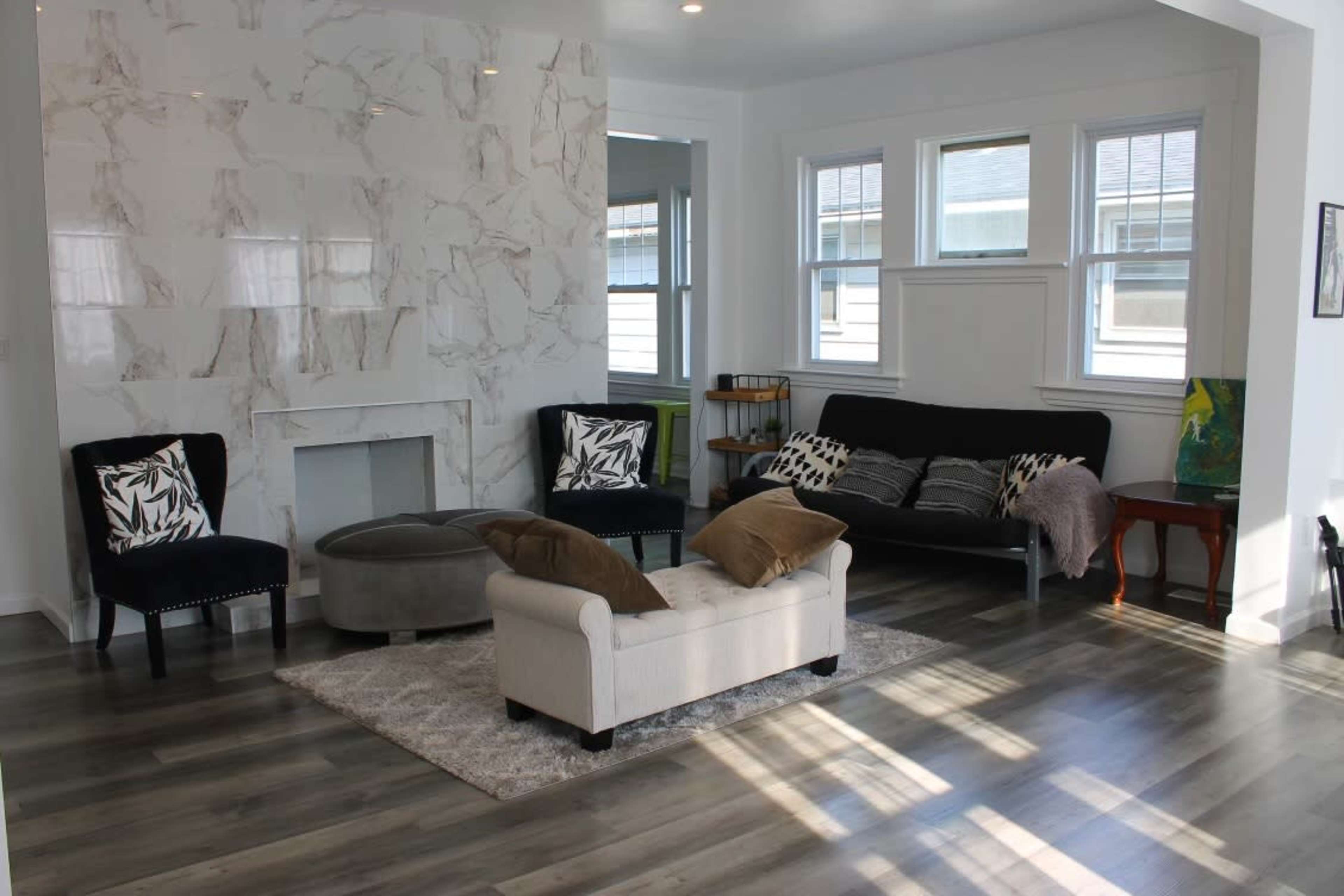 A modern living room with light wood flooring, a marble accent wall, a seating area consisting of a sofa and two chairs, and a small side table.