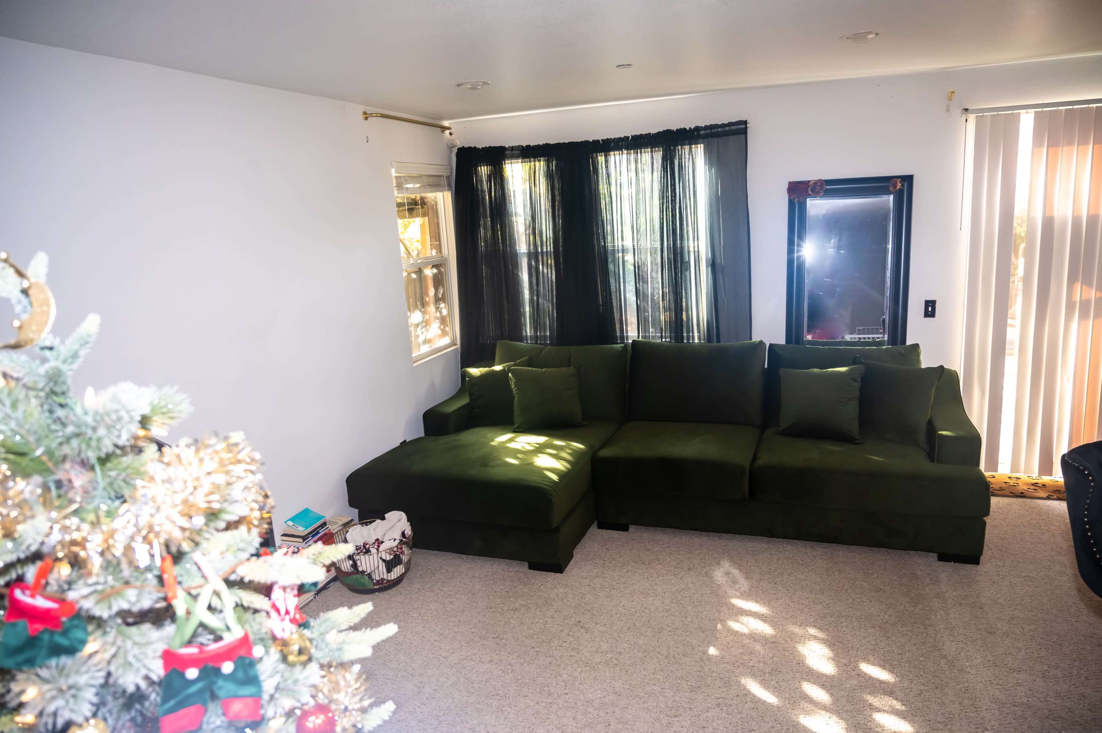 A green sectional sofa positioned in a brightly lit living room with large windows and a Christmas tree in the foreground.