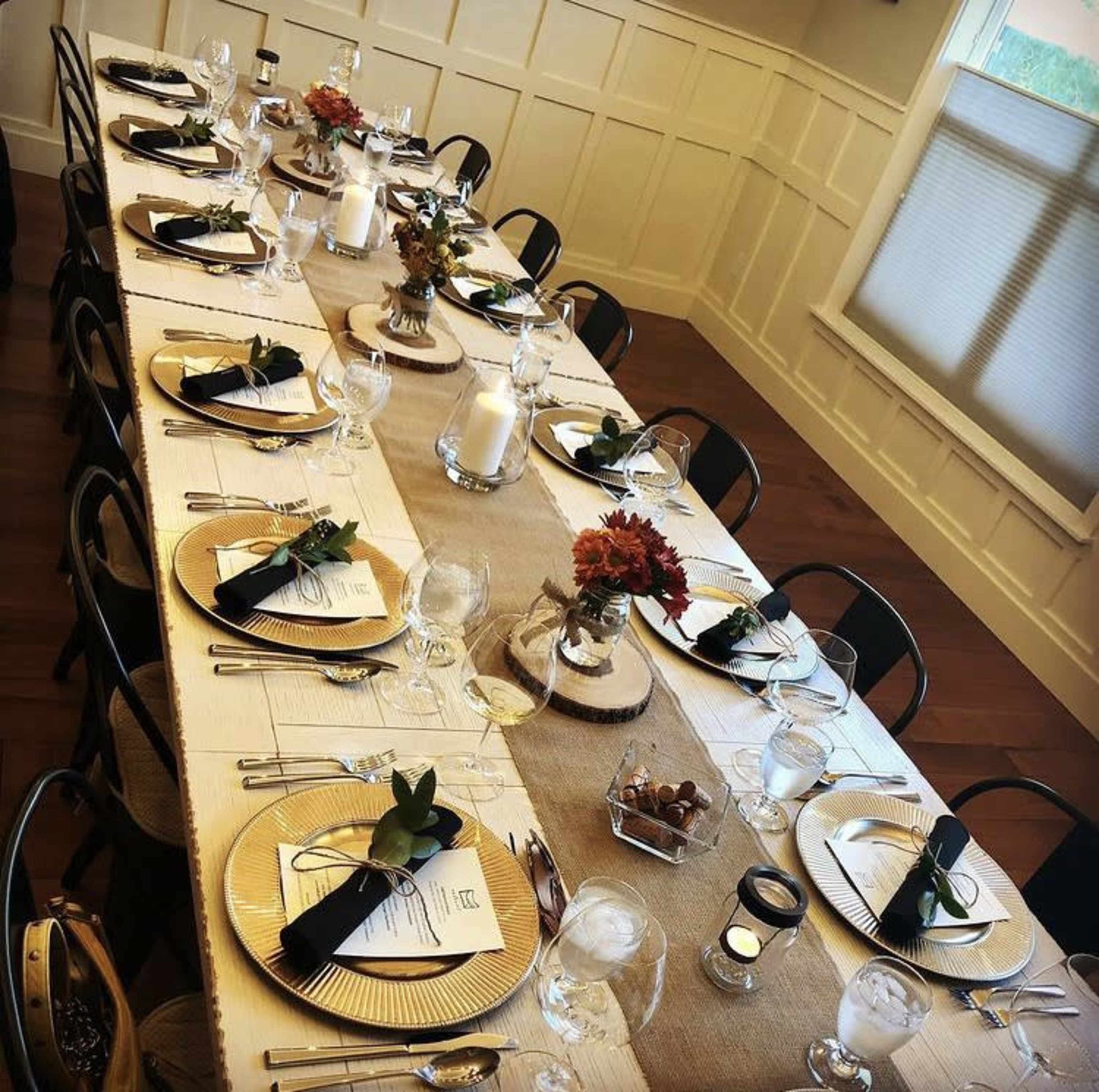 A long dining table is elegantly set with gold-rimmed plates, glassware, and centerpieces of flowers and candles.
