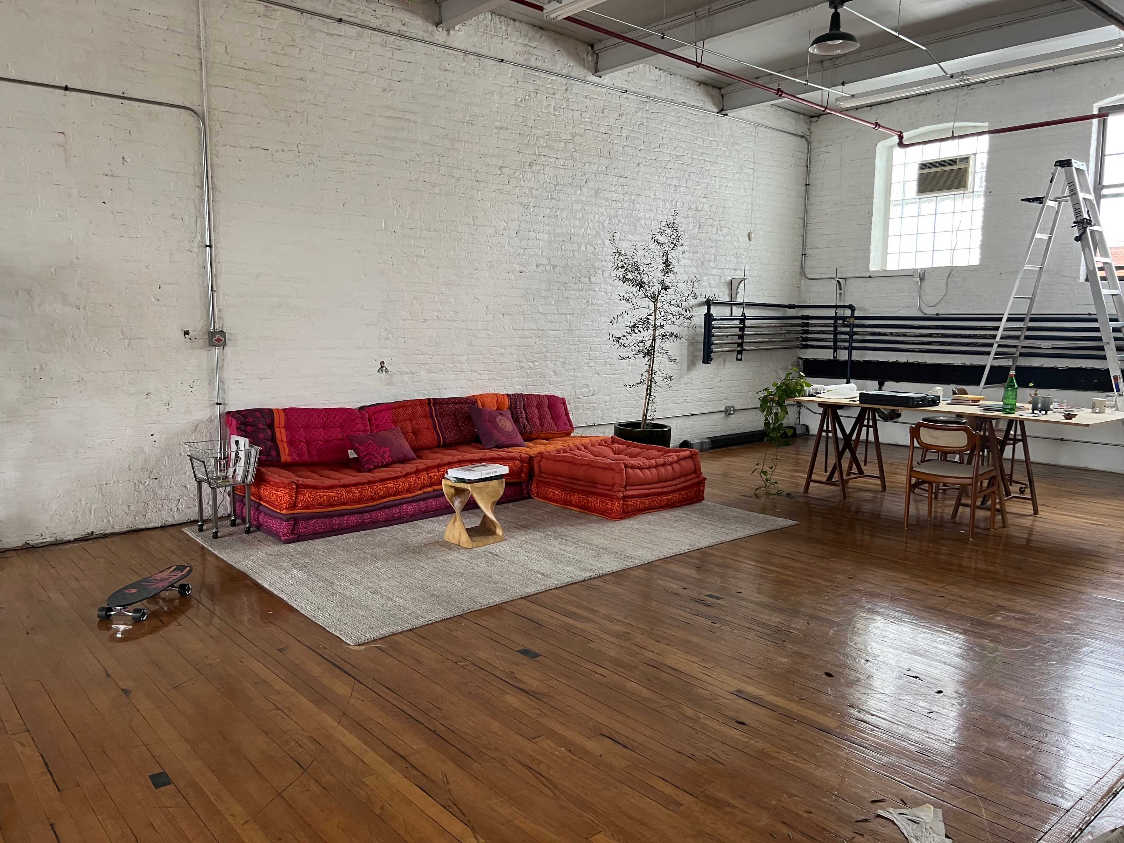 A spacious, minimalist room featuring a colorful sofa, a small wooden table, and a ladder against the wall.
