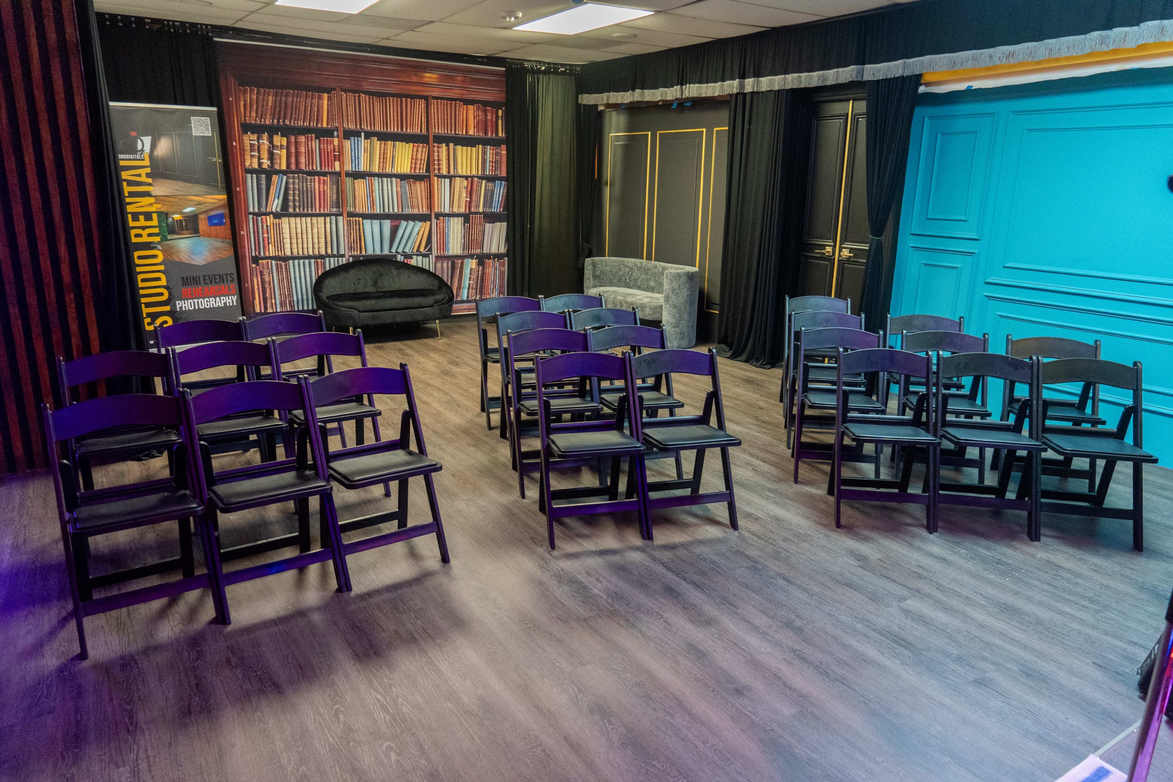 A room set up with neatly arranged black folding chairs facing a backdrop that resembles a bookshelf.