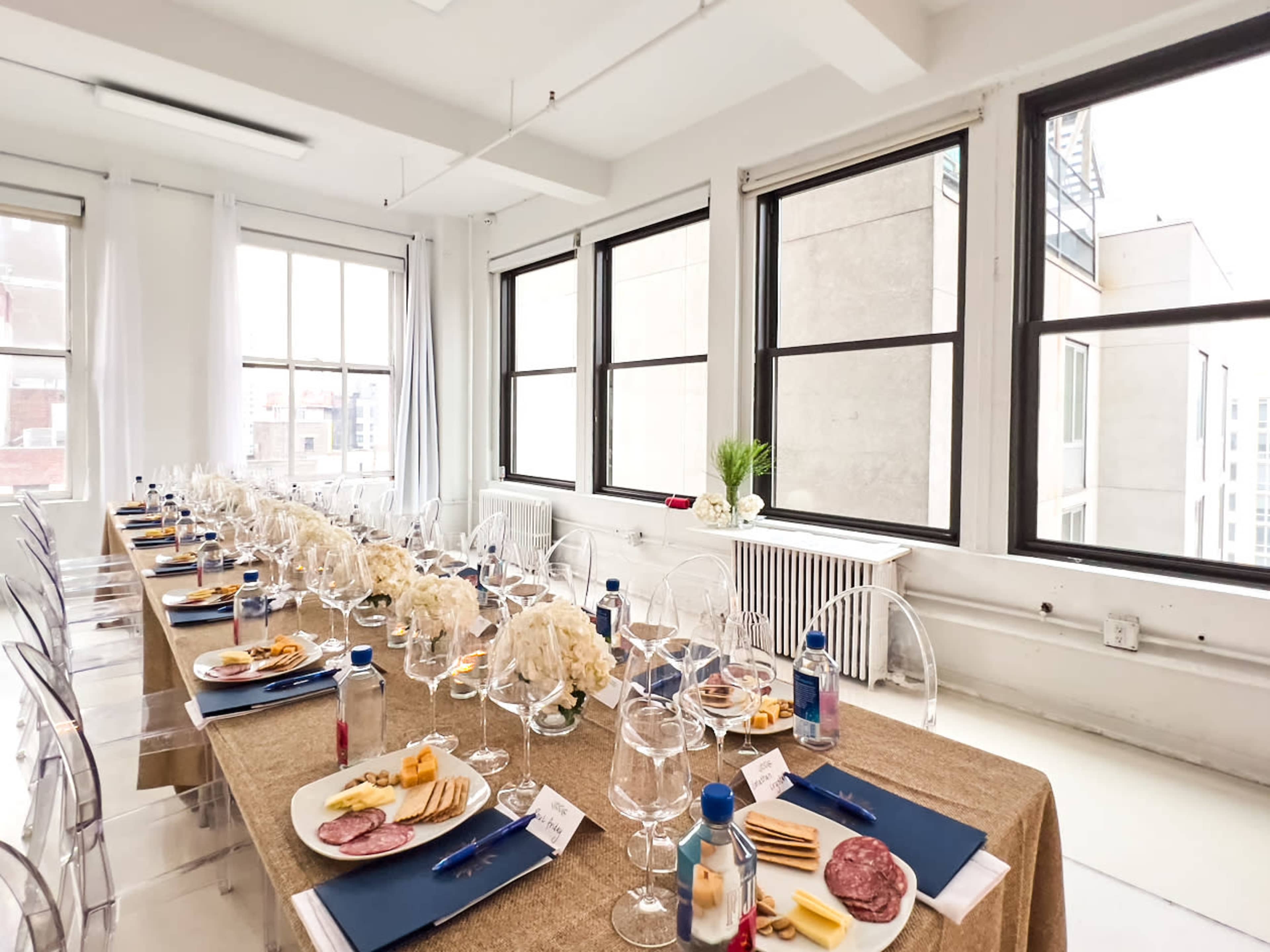 A long dining table is set with plates of food and glasses, surrounded by large windows that let in natural light.
