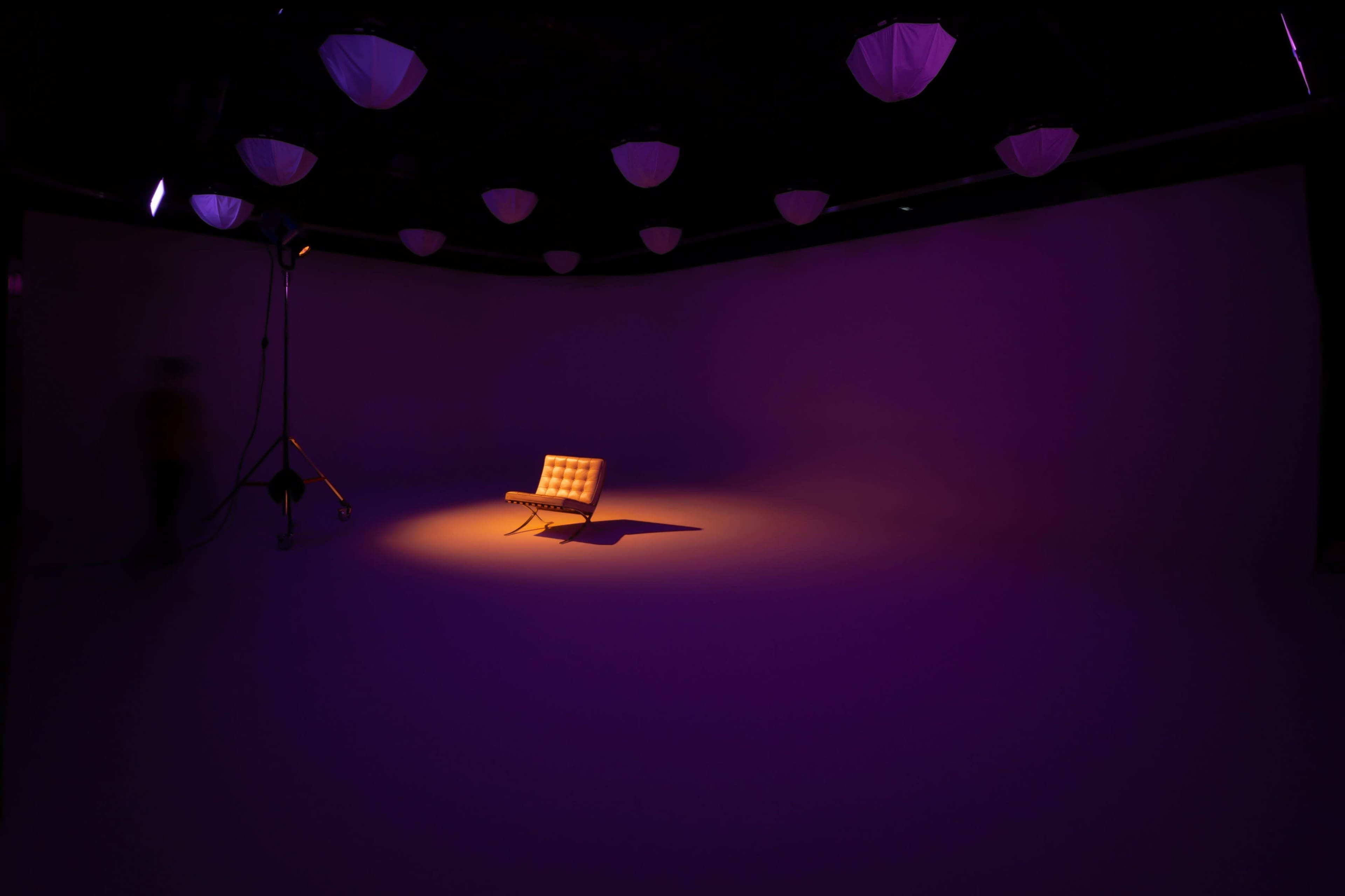 A solo chair is illuminated by a spotlight in a dimly lit studio with purple walls.