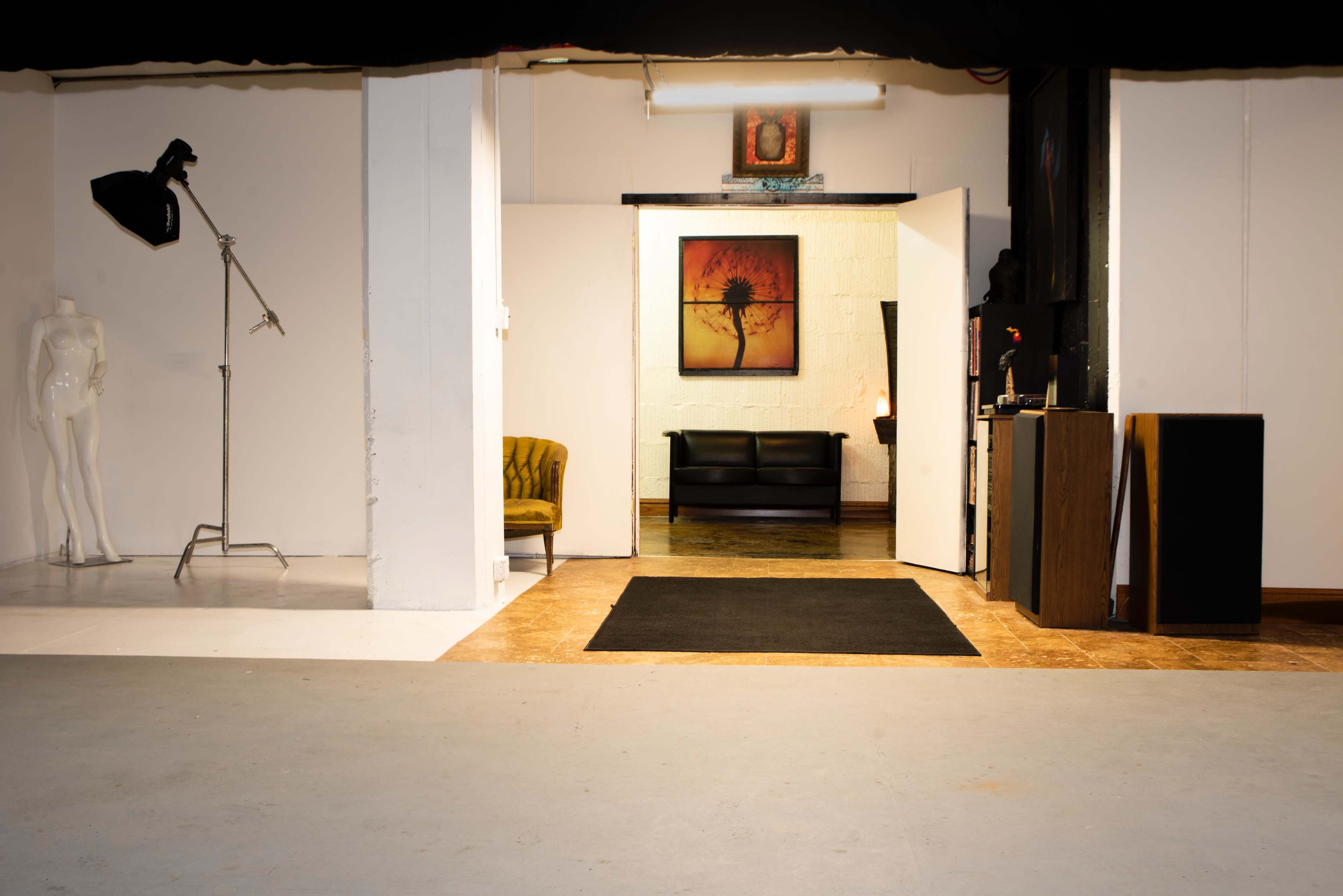 The image shows an open space leading into a room with a couch, artwork on the wall, and a mannequin near a lighting stand.
