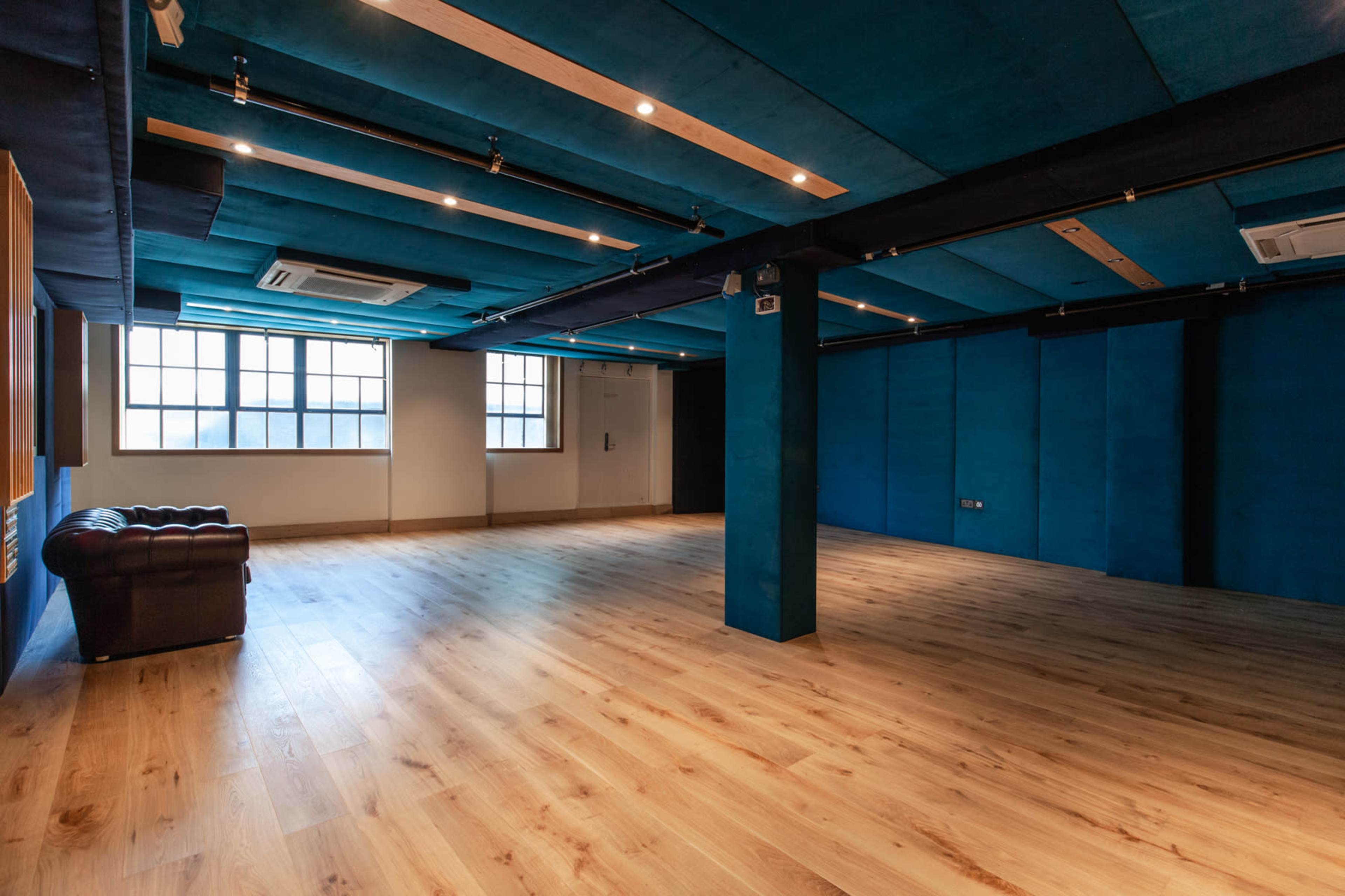 An empty room with blue walls, wooden flooring, and a brown leather sofa situated against one wall.