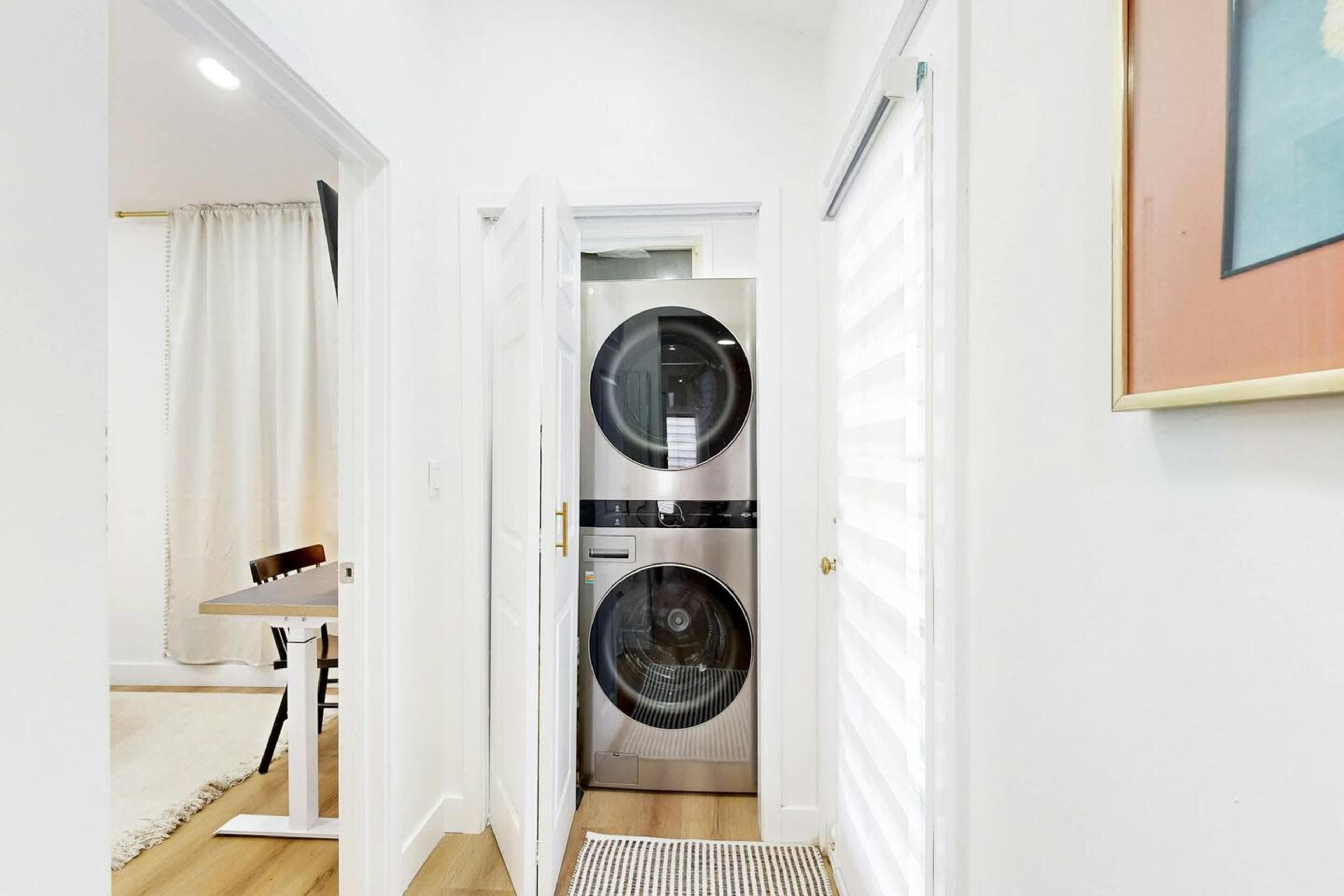 A stacked washer and dryer are placed in a narrow hallway beside a door leading to another room.