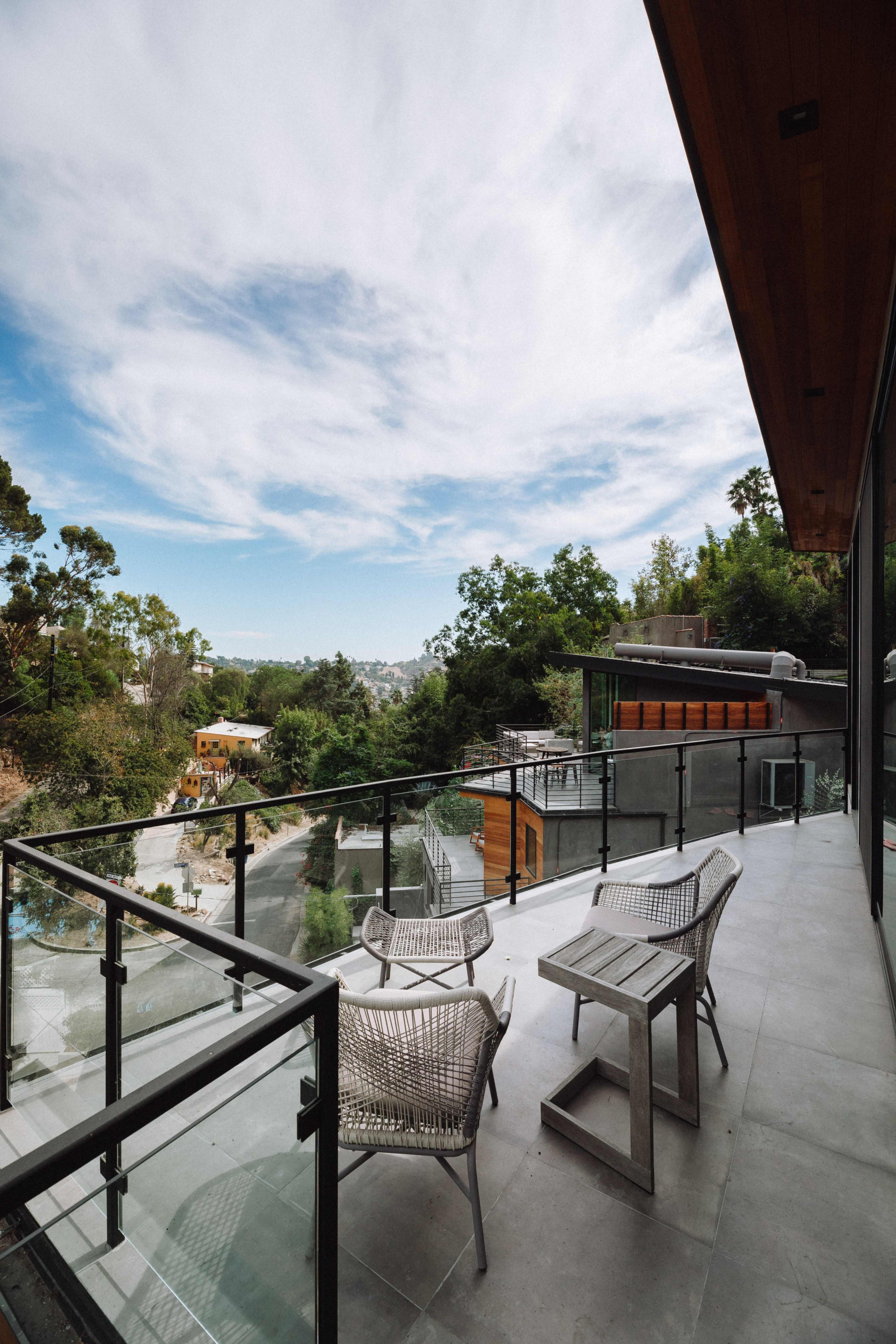 A modern balcony features minimalist furniture and a clear view of a tree-lined hillside.