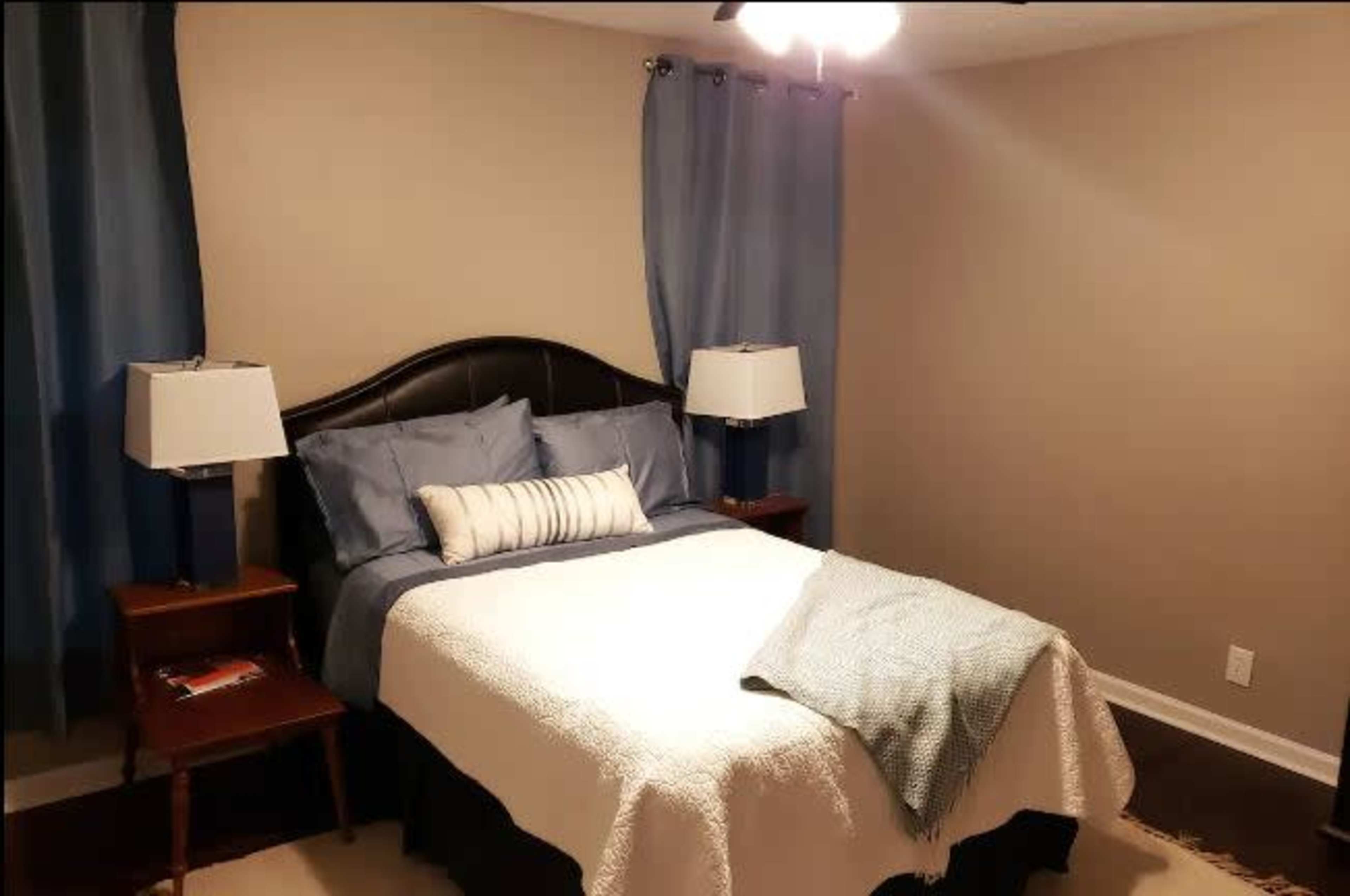 A neatly arranged bedroom with a bed, blue curtains, two bedside lamps, and a decorative throw blanket.