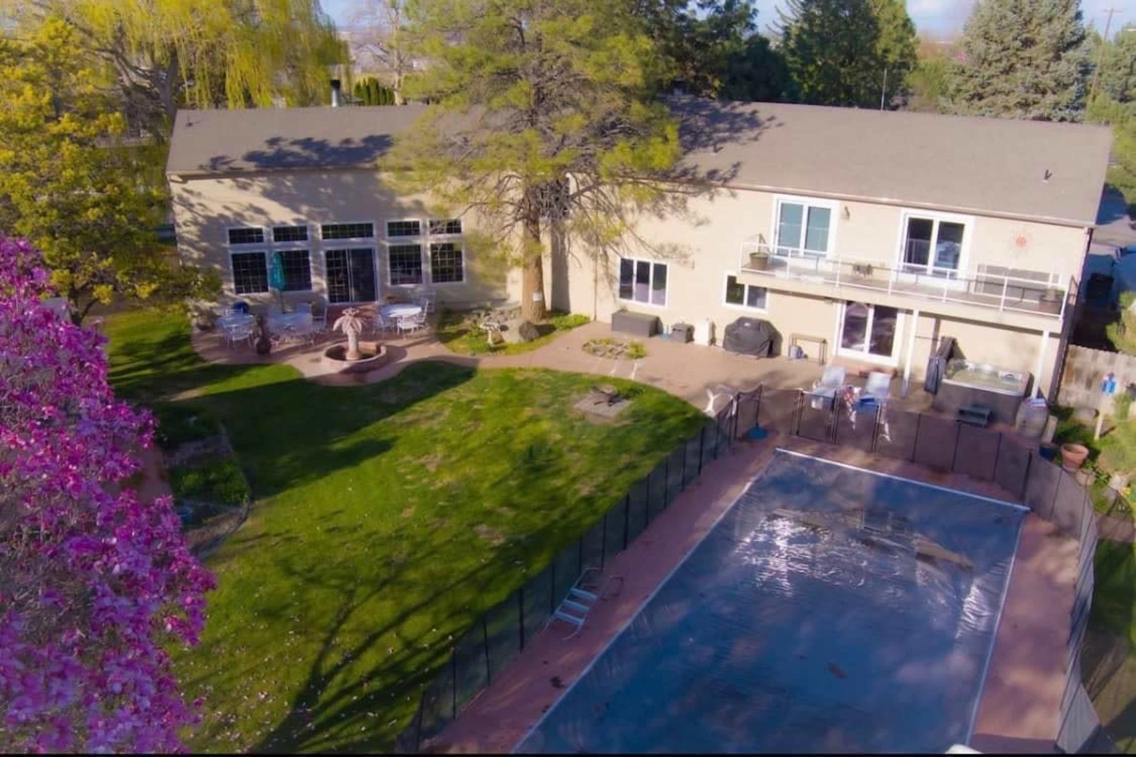 The aerial view shows a house with a pool surrounded by a fenced yard, featuring a patio area and trees.