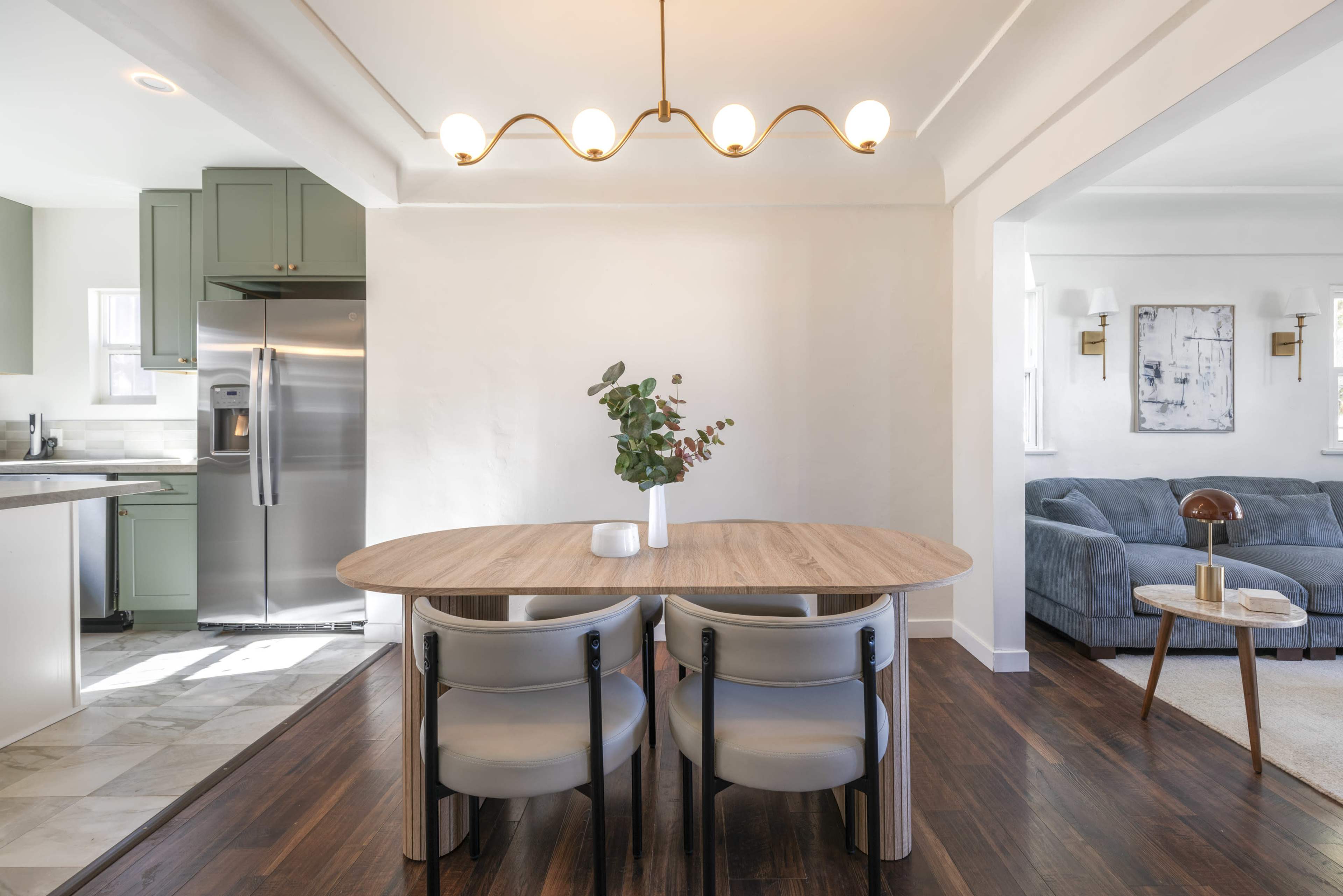 A modern dining area features a round wooden table surrounded by two chairs, with a kitchen visible in the background.