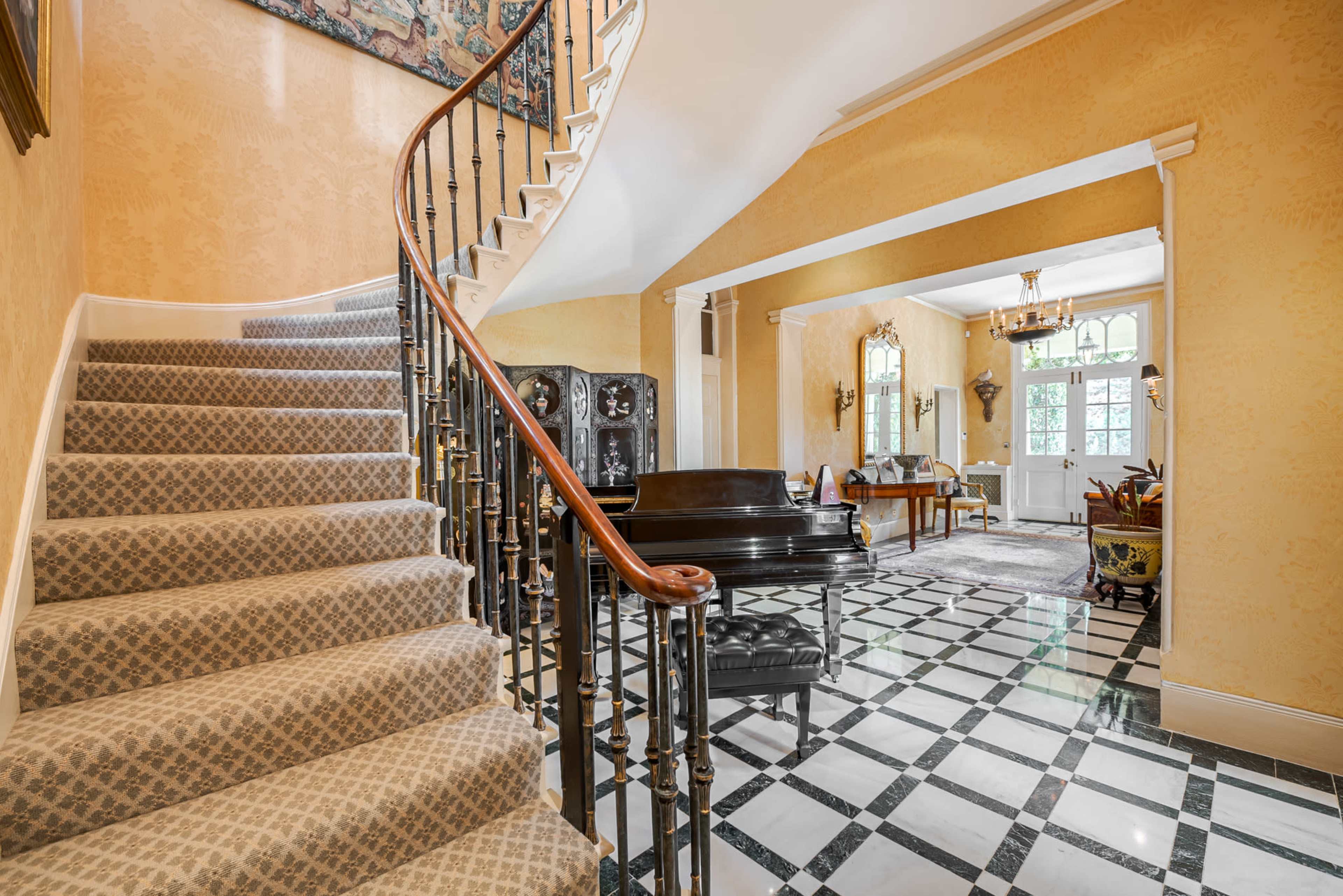 A curved staircase leads to an upper level, with a checkered black and white floor in a spacious foyer that opens into a living area.