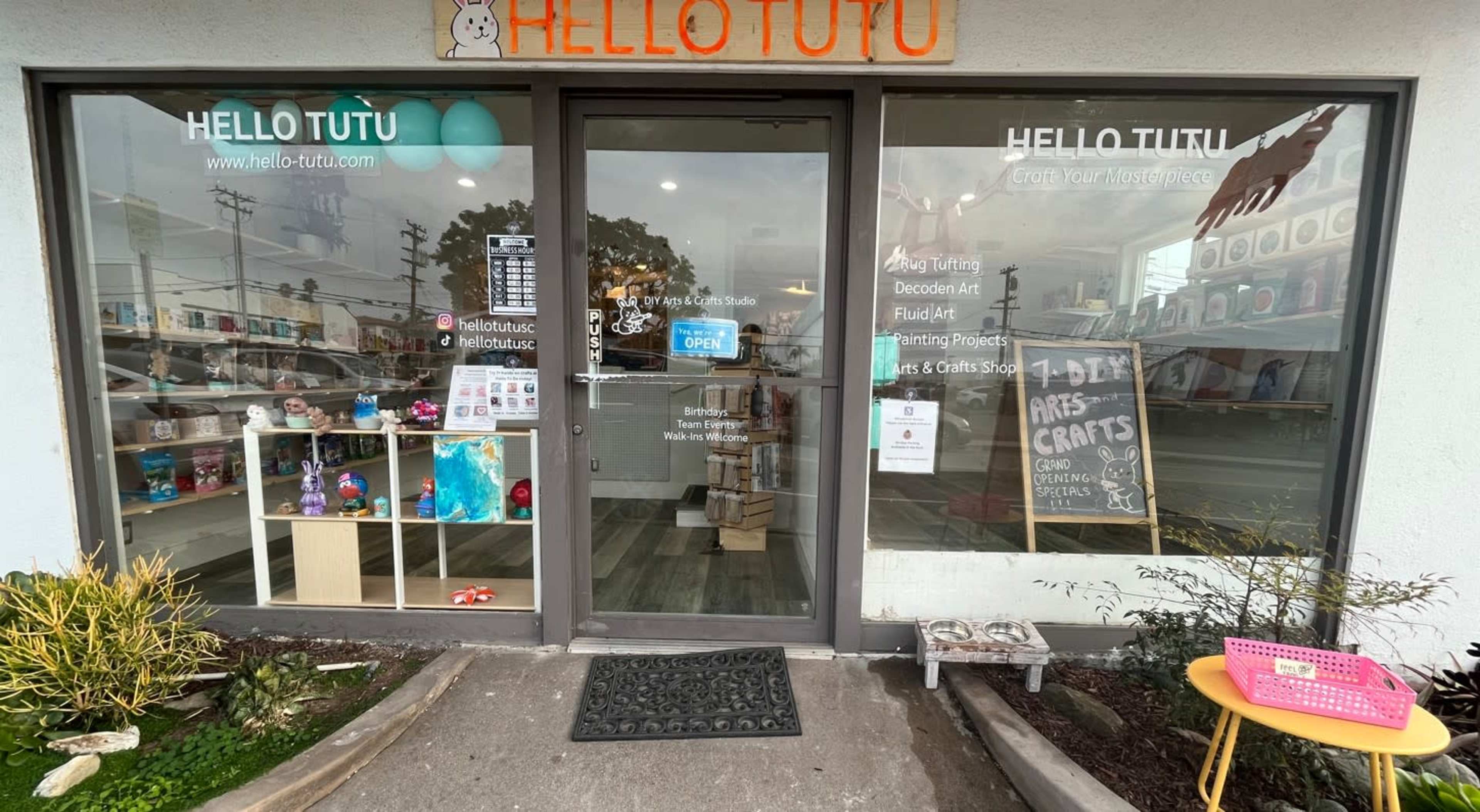 The image shows the entrance of a store named "Hello Tutu," featuring a glass door with an open sign and various crafts and art supplies displayed inside.