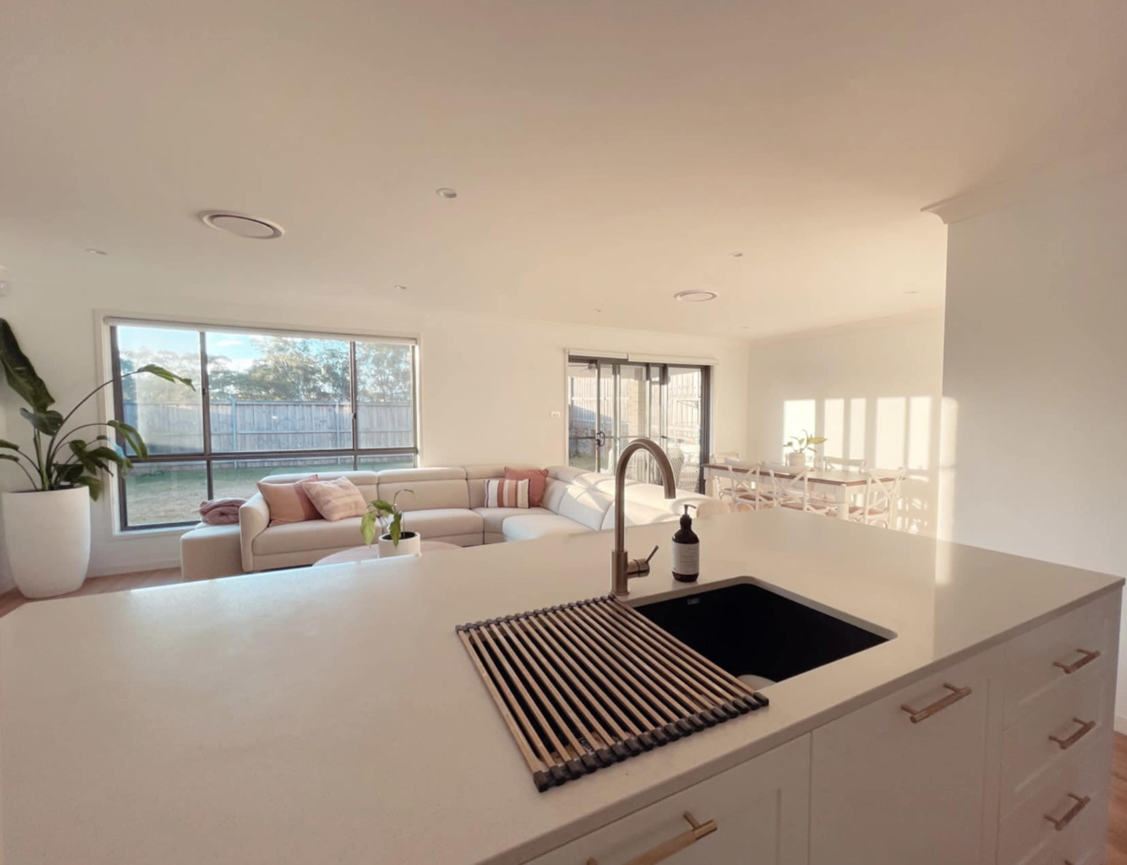 A modern kitchen features a sink and a view into a bright living area with a comfortable sofa and dining space.