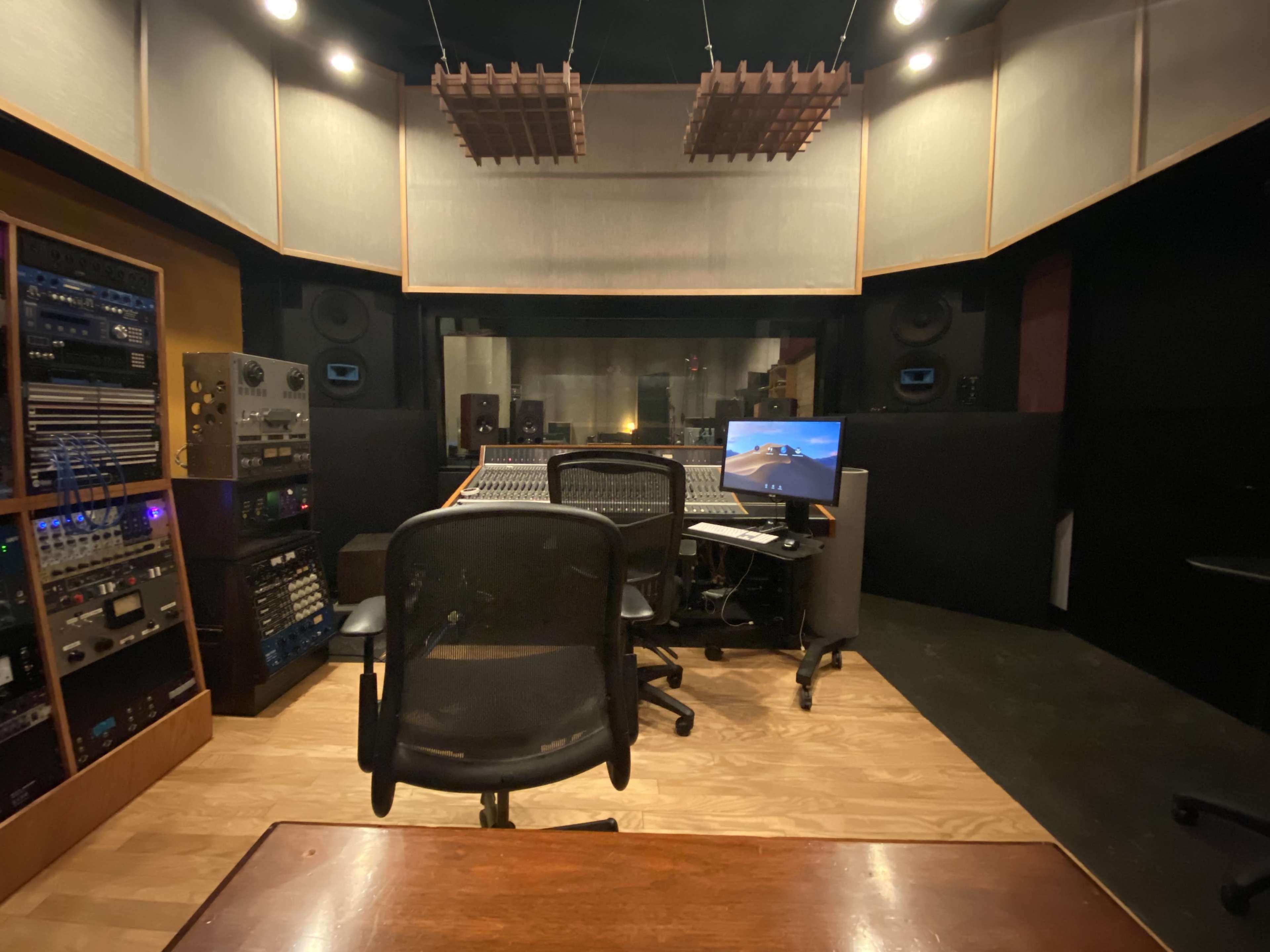 A sound recording studio with a large mixing console, computer, and audio equipment arranged in a semi-circular layout.