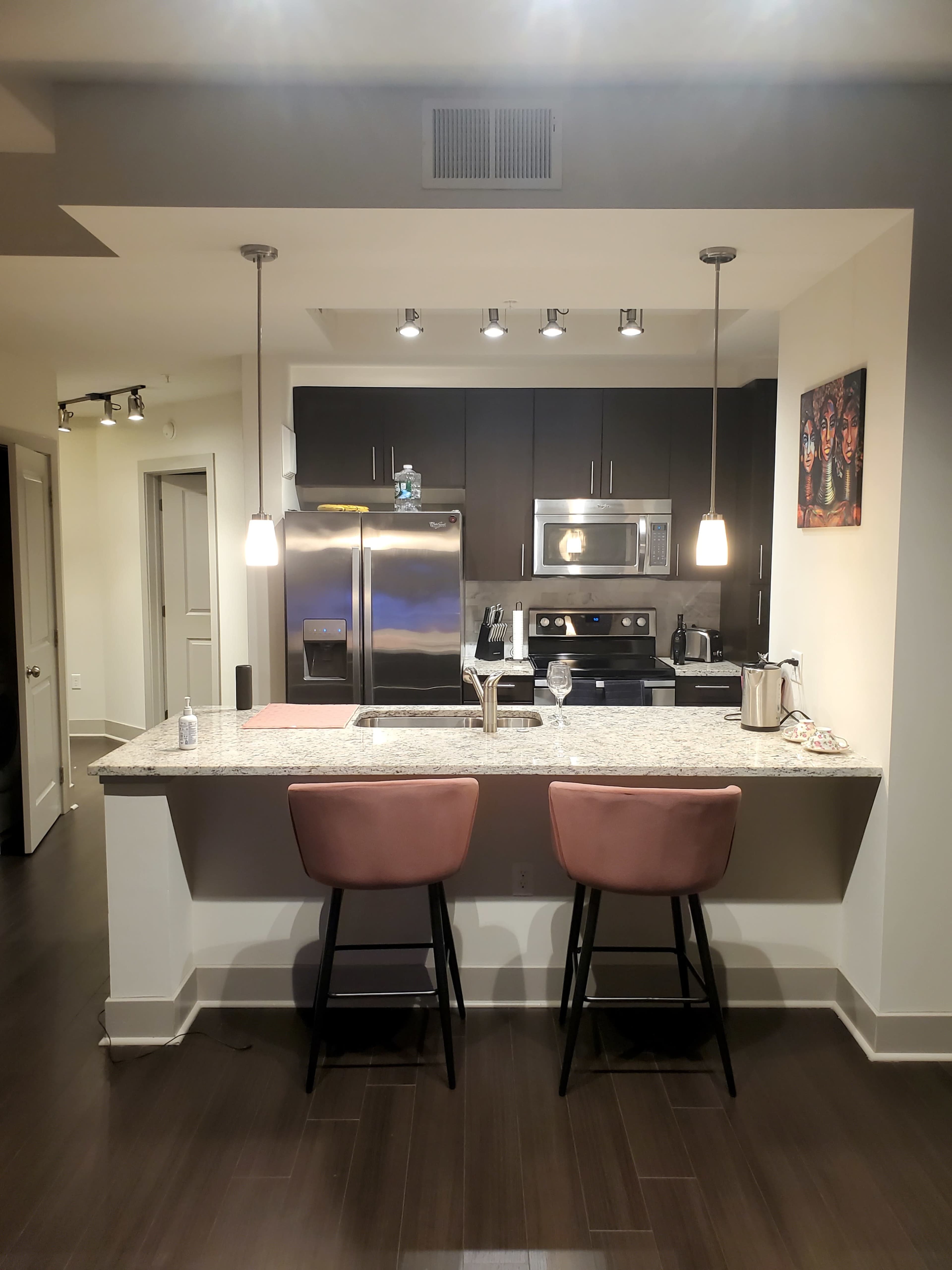 A modern kitchen with dark cabinets, granite countertops, and two pink bar stools at a counter island.
