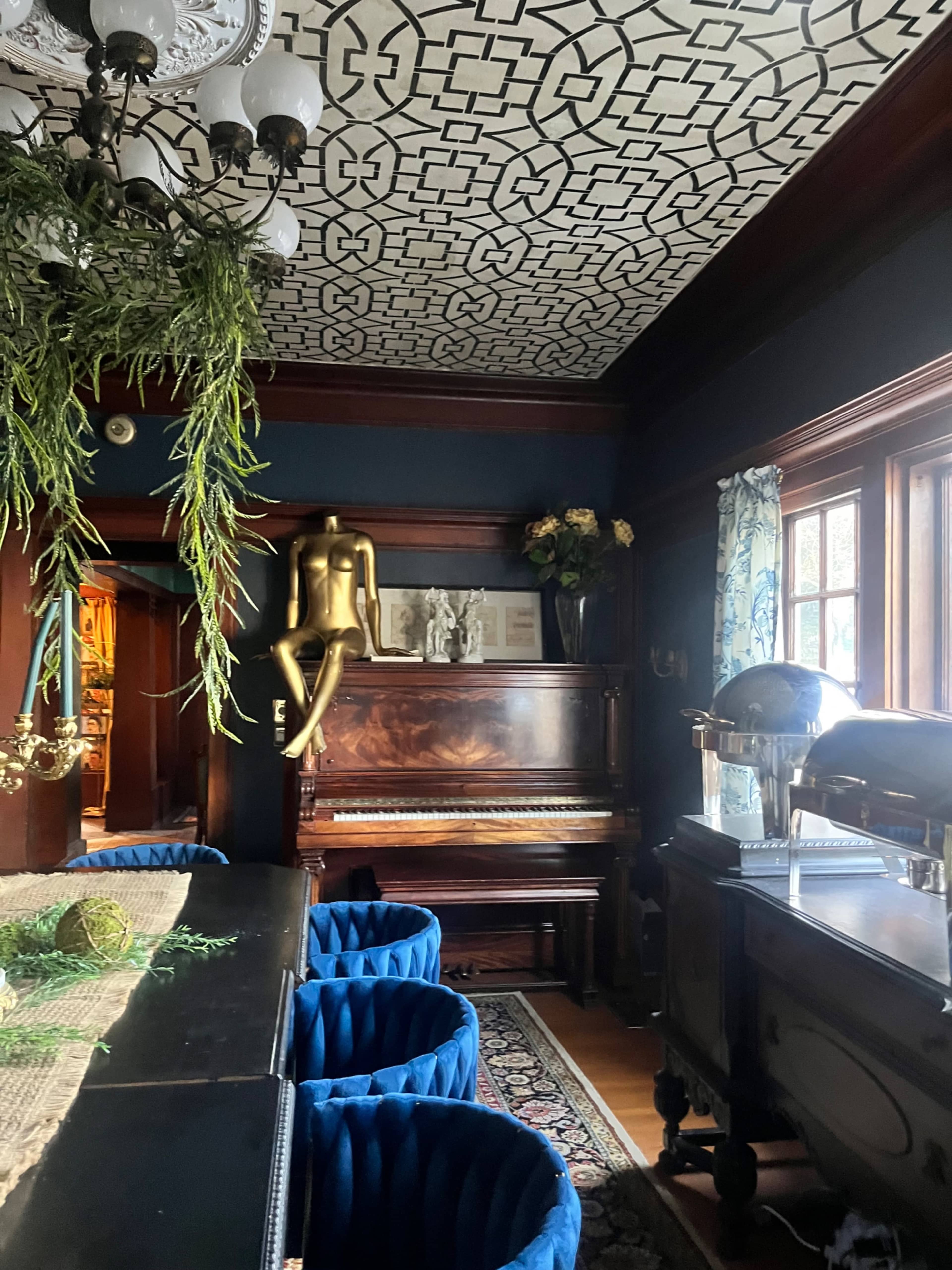 The room features a wooden piano next to a gold statue, with blue velvet chairs and an intricately patterned ceiling.