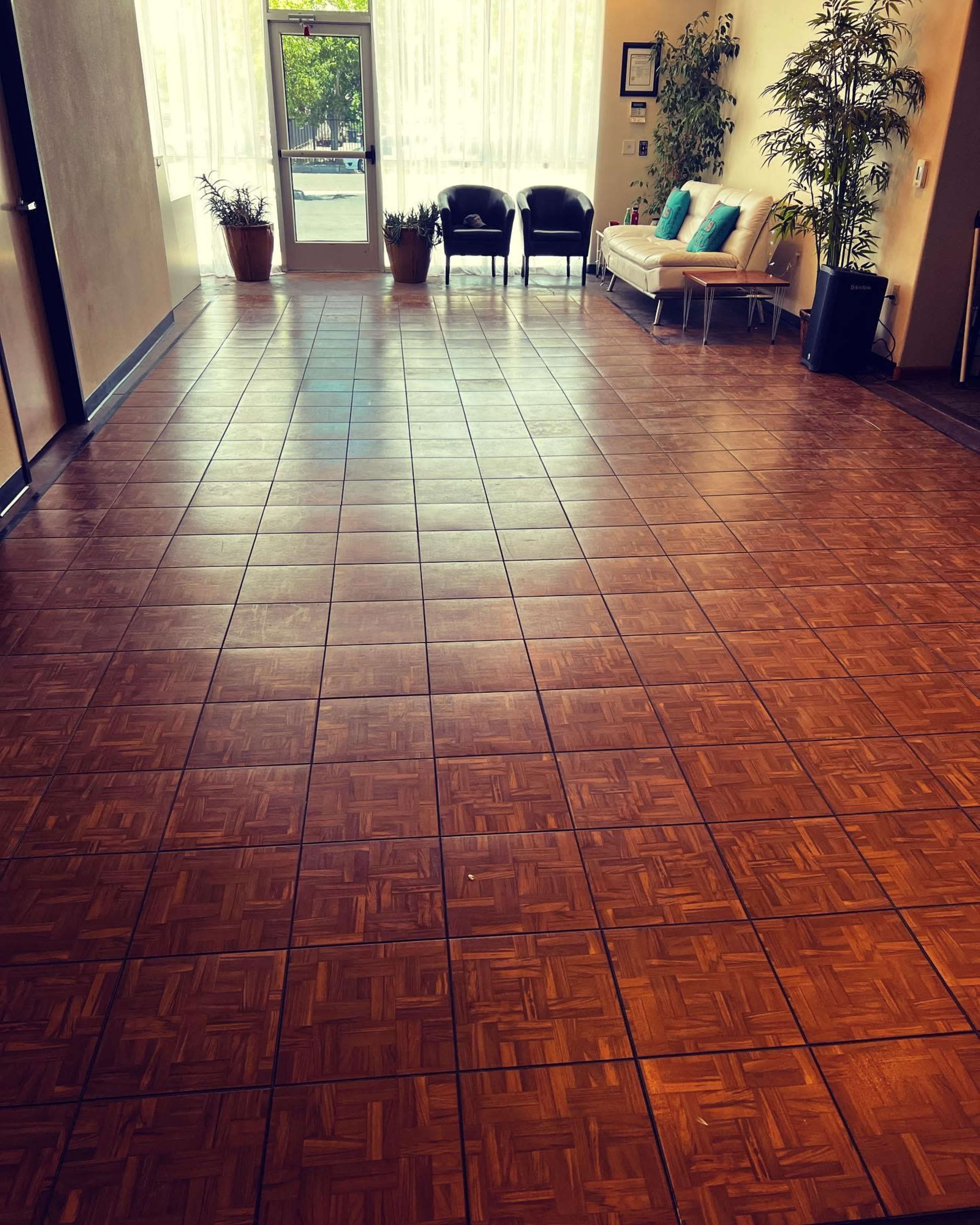 A spacious lobby area with a tiled floor, two chairs, a sofa, and plants near the windows.