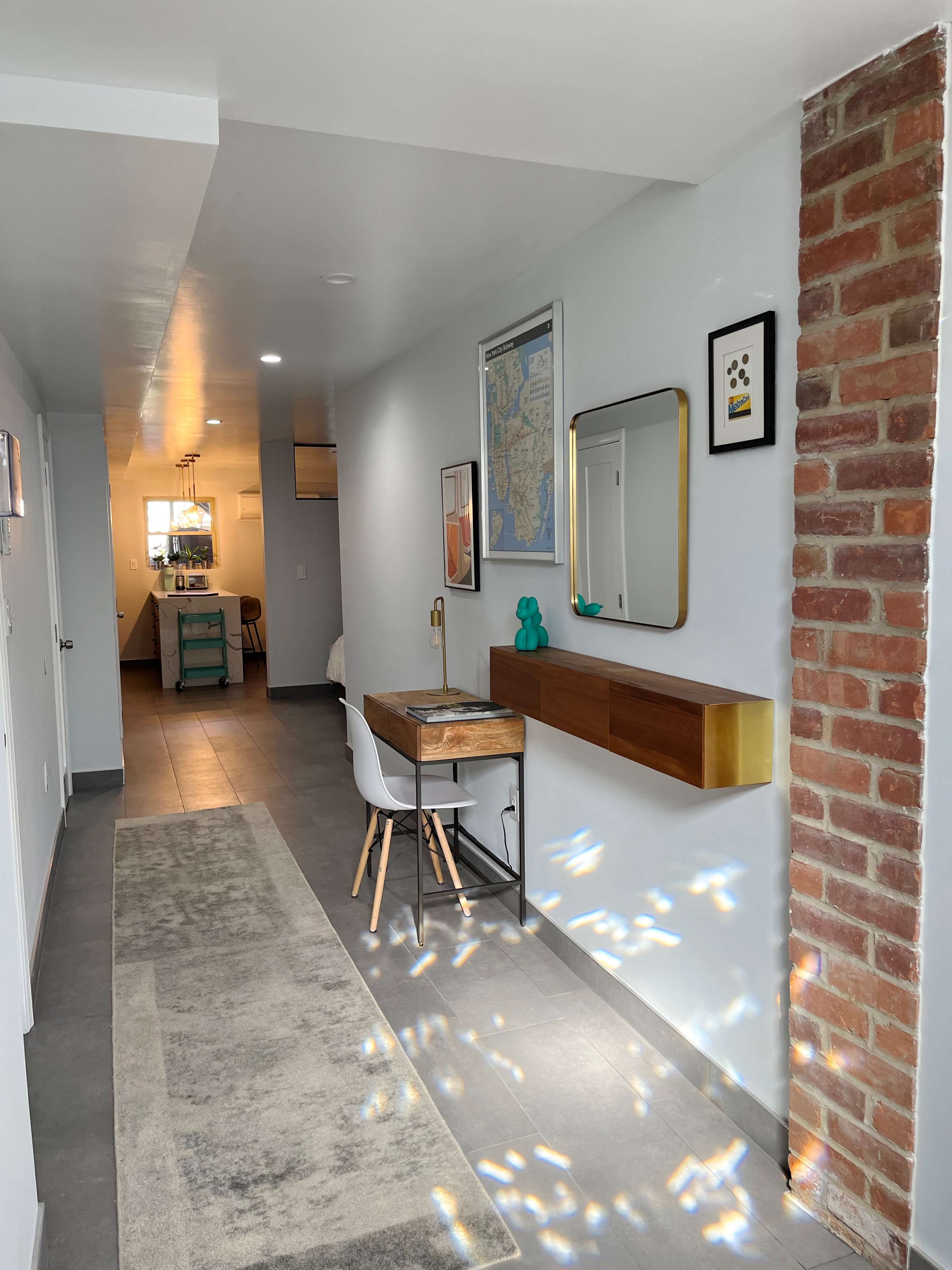 A well-lit hallway featuring a desk with a lamp, a mirror, and a wall with a brick section.