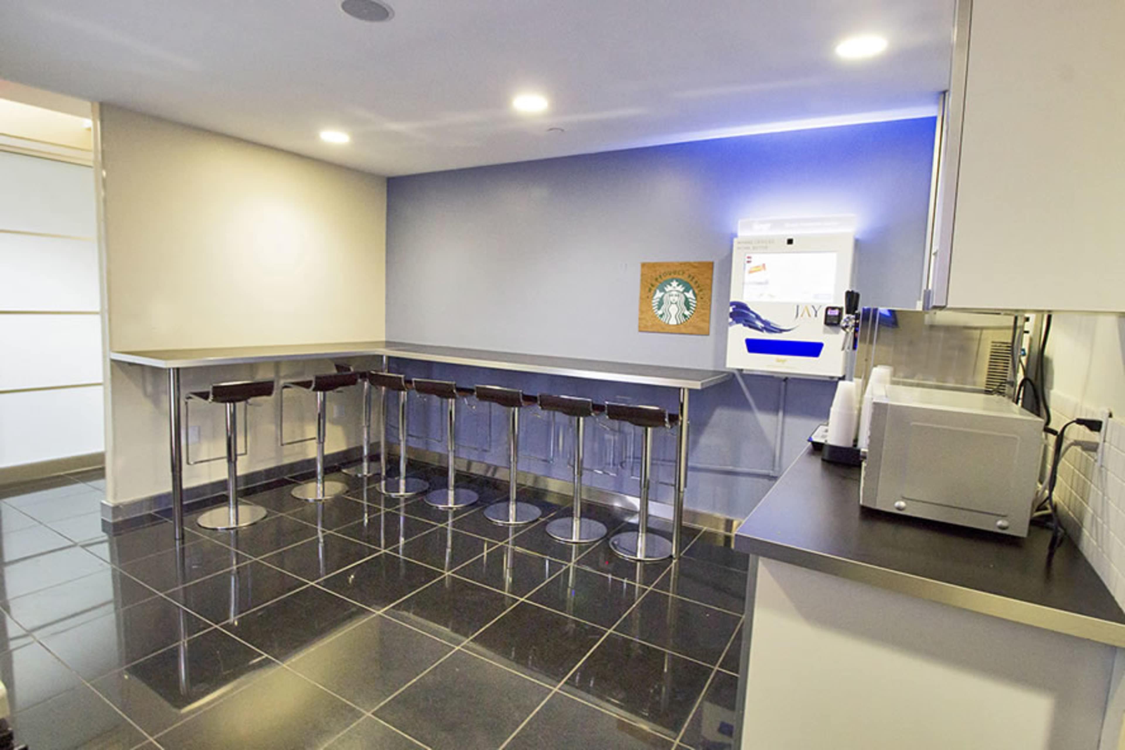 The image shows a modern kitchen area featuring a countertop with high stools, a coffee machine, and a wall-mounted Starbucks sign.