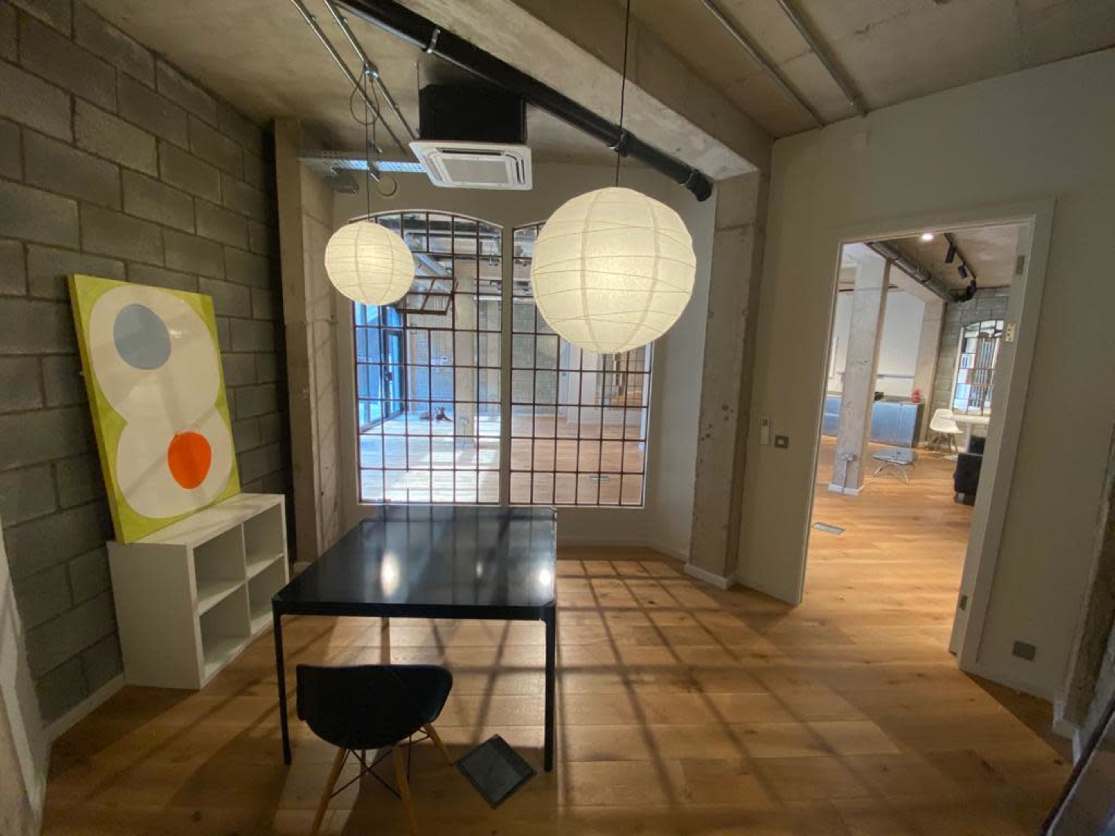 A well-lit room featuring a black table and an abstract painting alongside paper lanterns hanging from the ceiling.