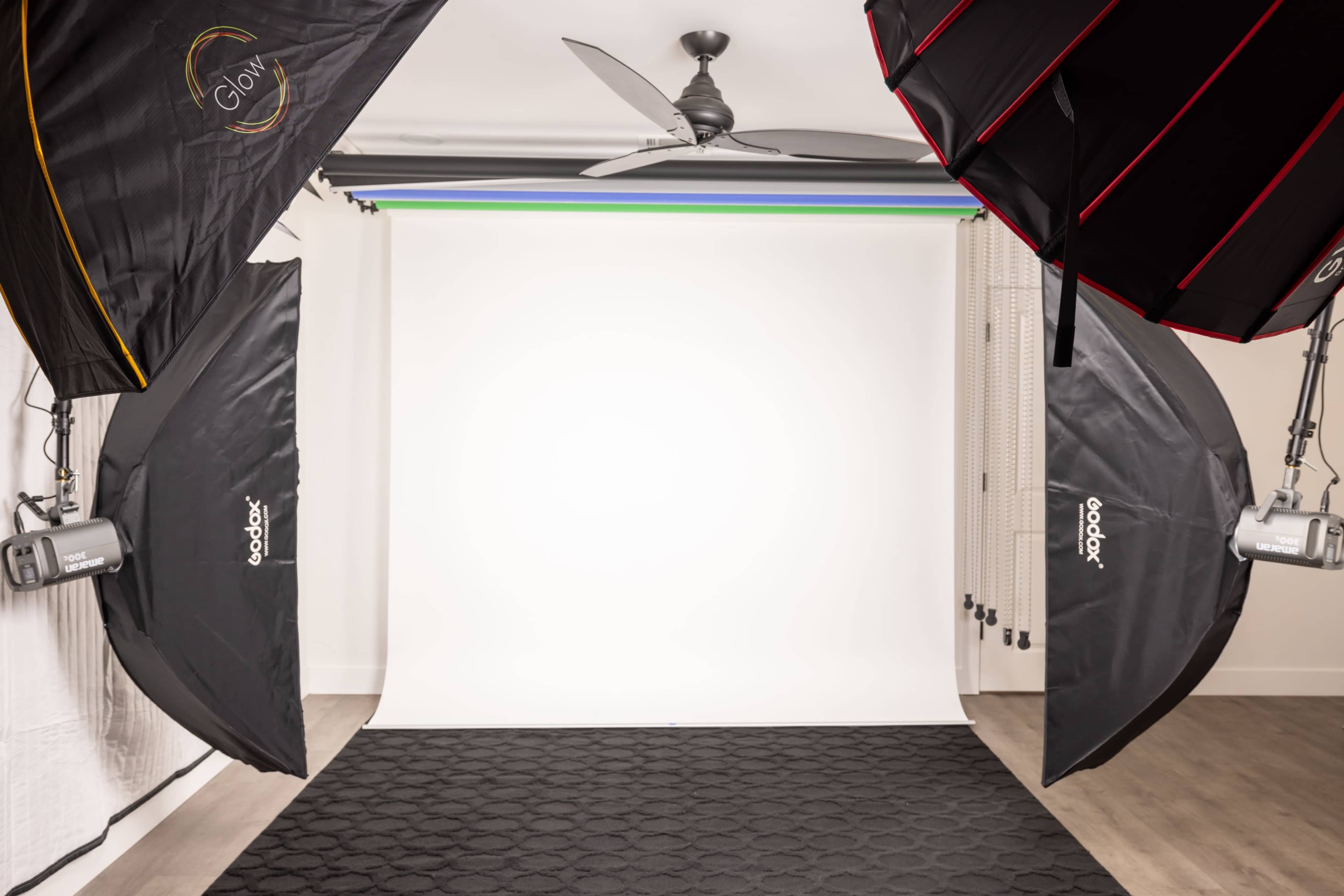 The image shows a photography studio setup with two large softbox lights illuminating a blank background.