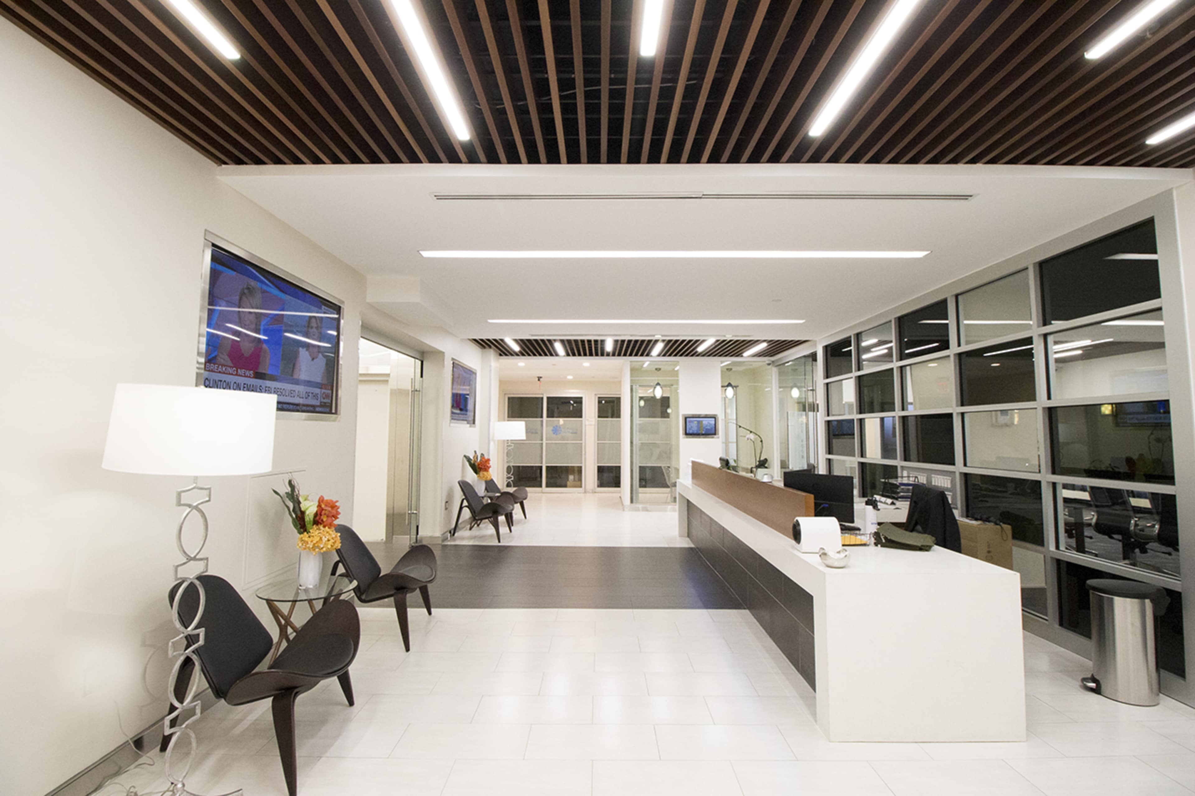 A modern lobby area with a reception desk, seating chairs, and large windows, illuminated by overhead lighting.