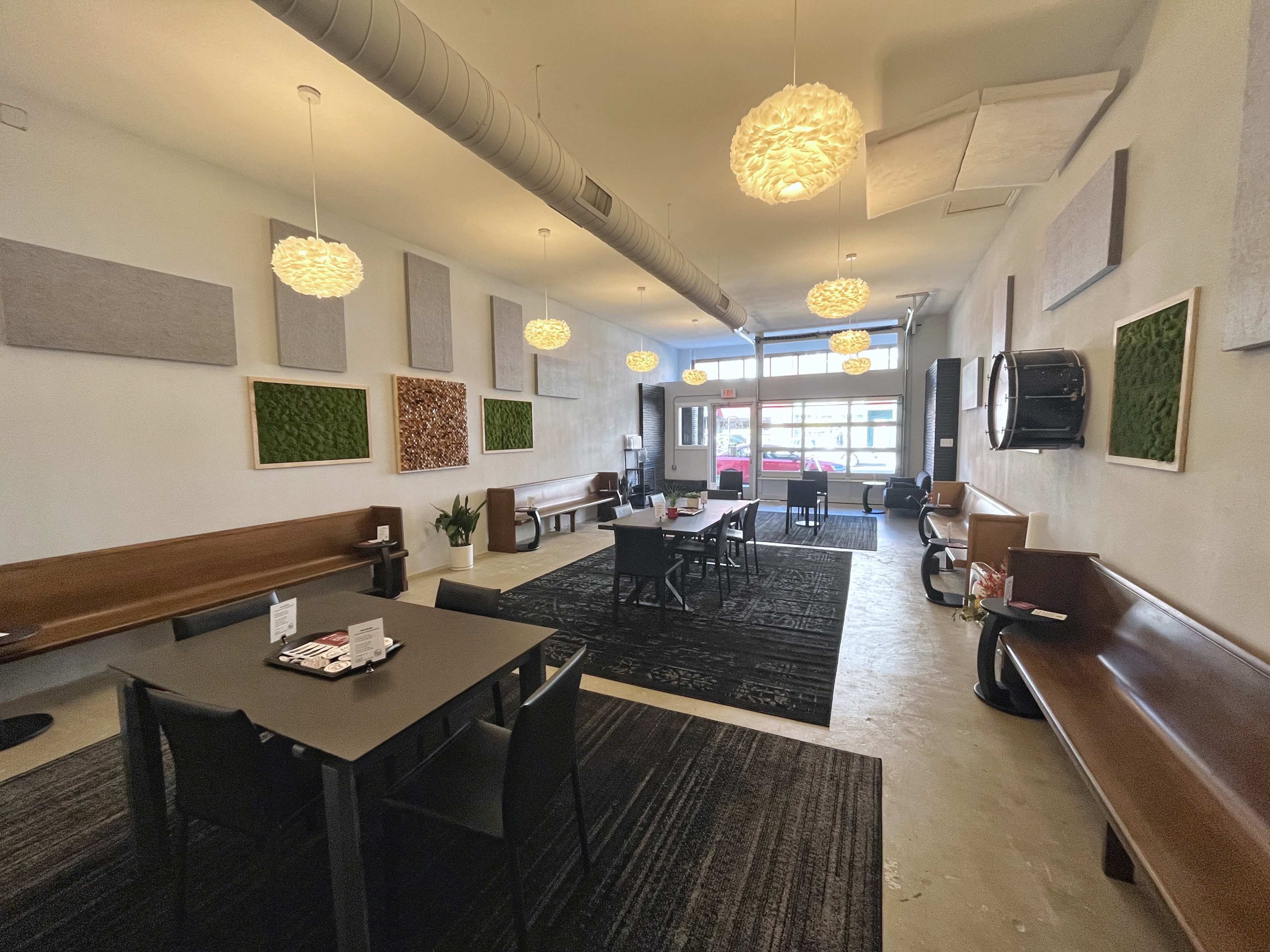 A spacious modern interior of a café with wooden seating, black tables, and decorative light fixtures hanging from the ceiling.