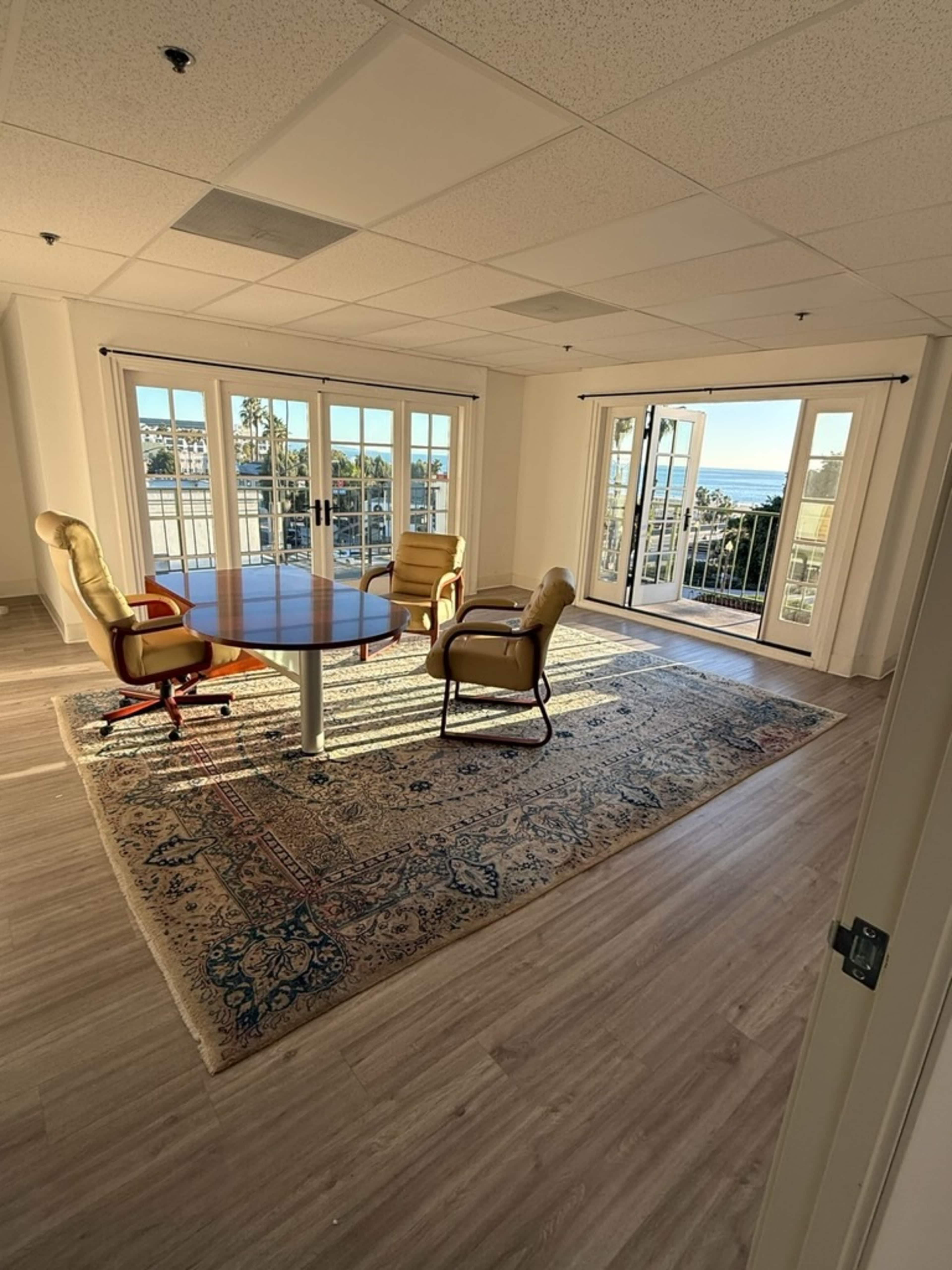 A conference room features a round table surrounded by four chairs and large windows that provide a view of the outdoors.