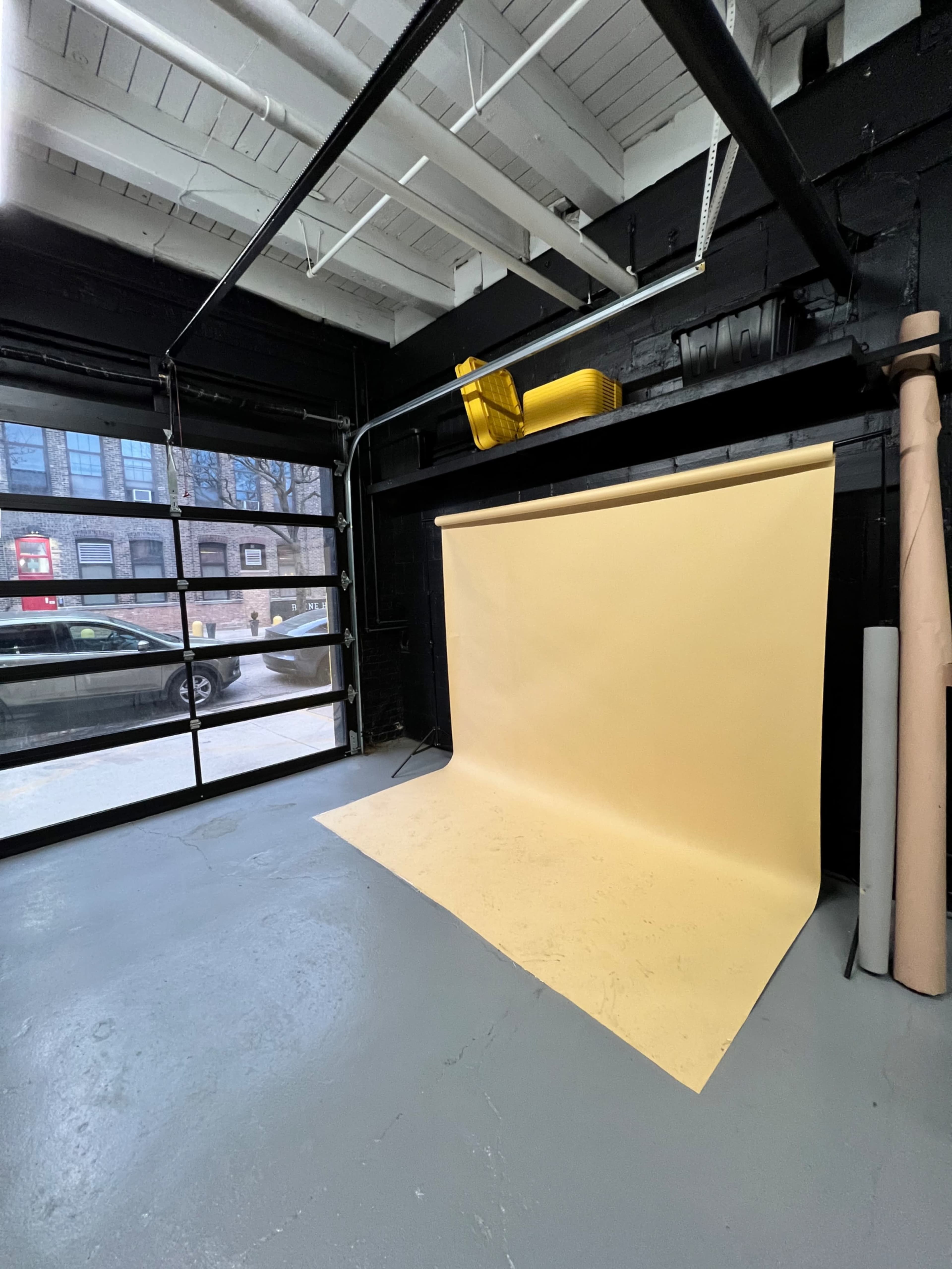 A studio space with a yellow backdrop and a large garage door partially open, revealing a glimpse of an exterior scene.